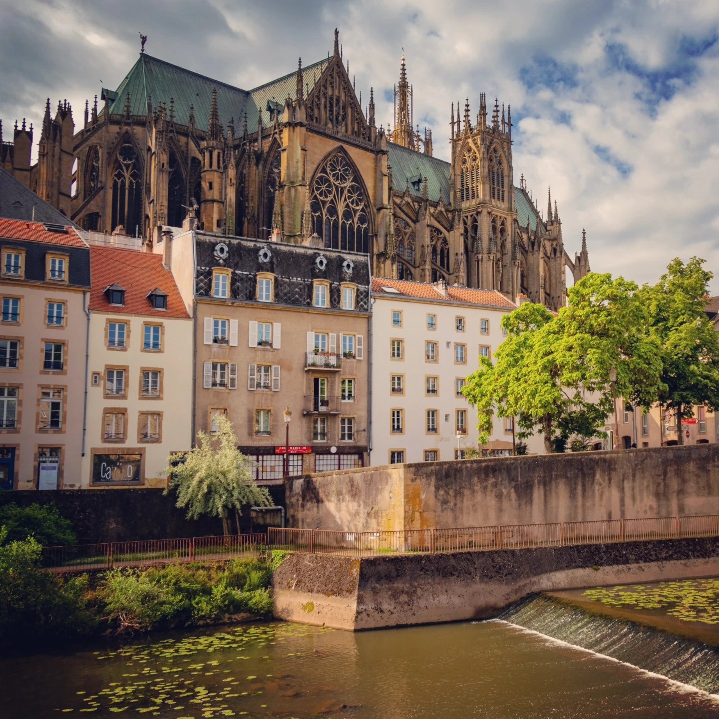 View of Metz Cathedral towering above houses near the riverbank.