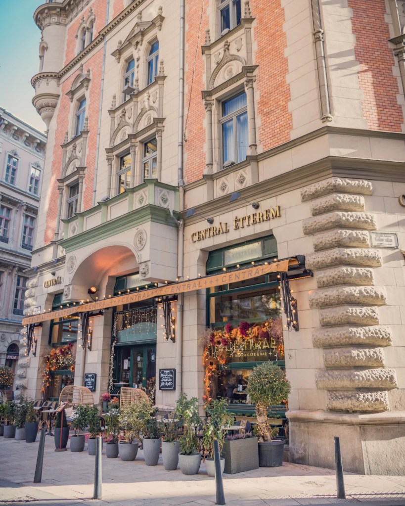 The facade of Centrál Grand Café & Bar in Budapest, with holiday flowers, warm lighting, and a mix of brick and stone architectural detail.