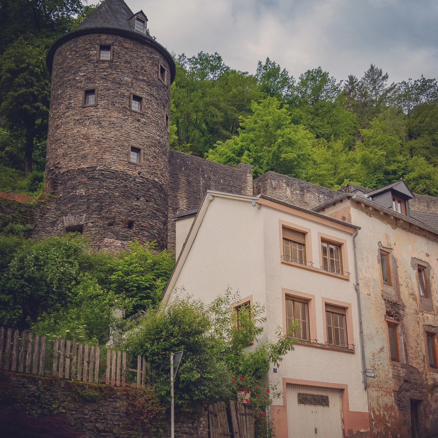 Round medieval stone tower rising above homes and greenery in Vianden, Luxembourg.