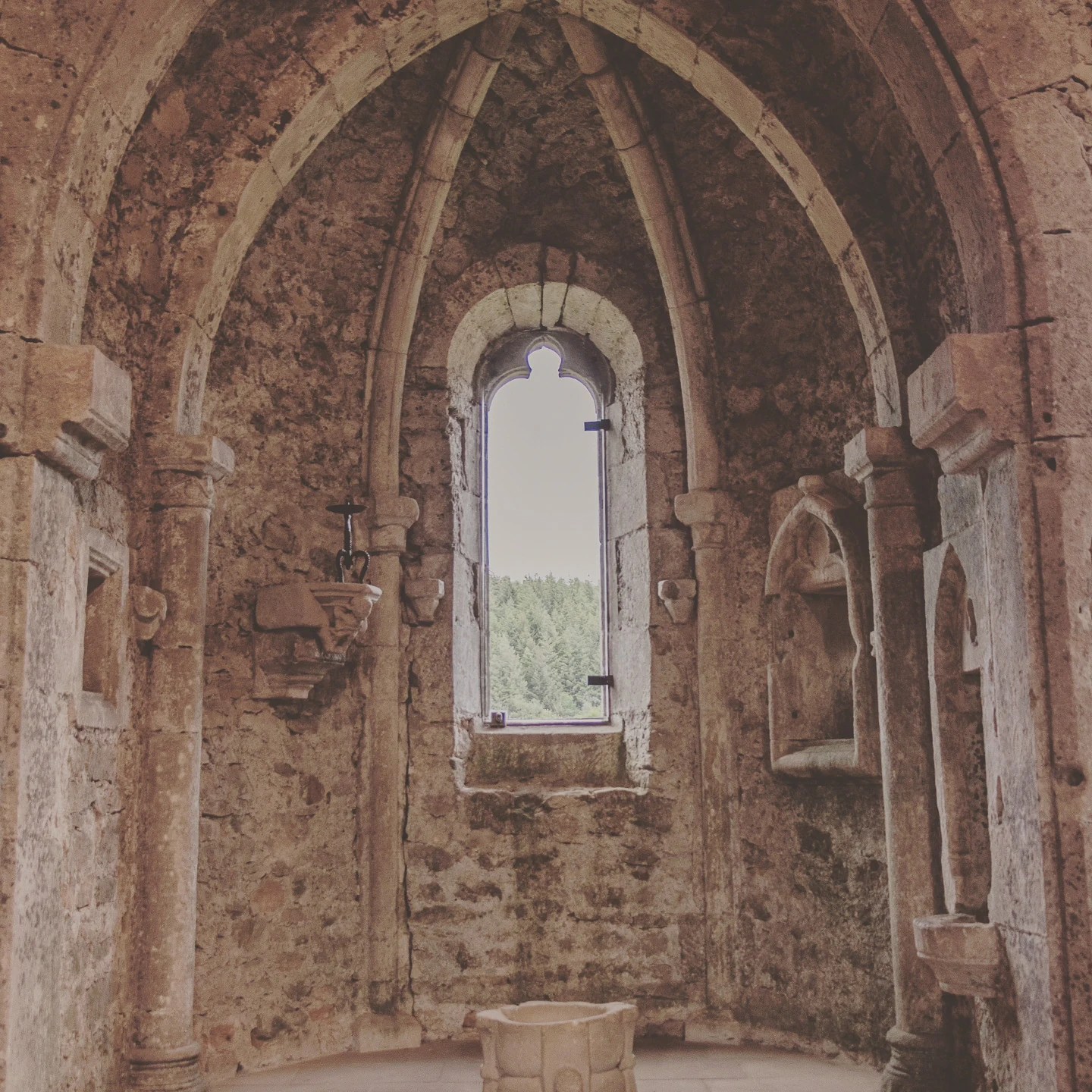 Gothic-style chapel interior with pointed arches and a central window at Larochette Castle.