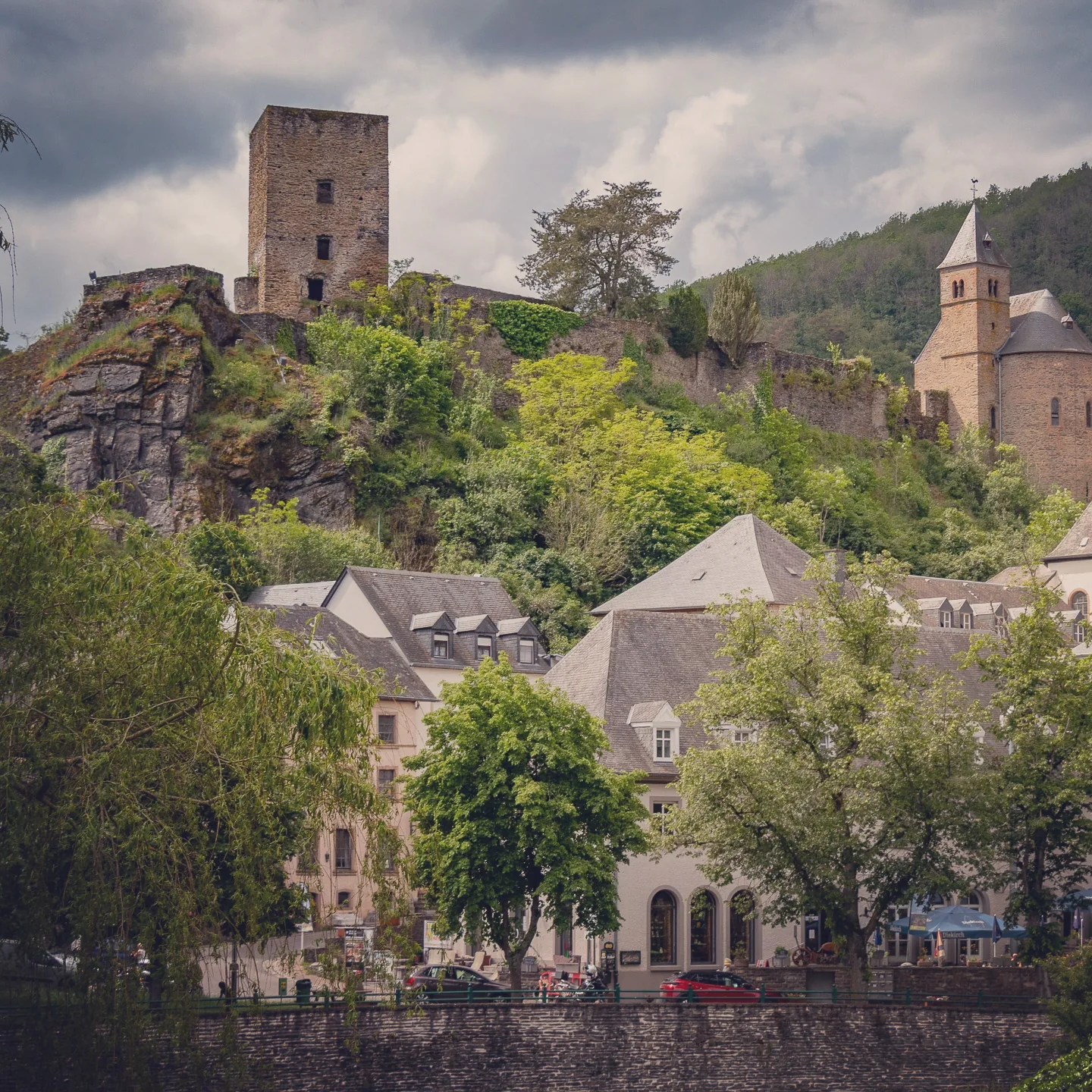 Stone ruins of Esch-sur-Sûre castle rising above the village rooftops and green hills.