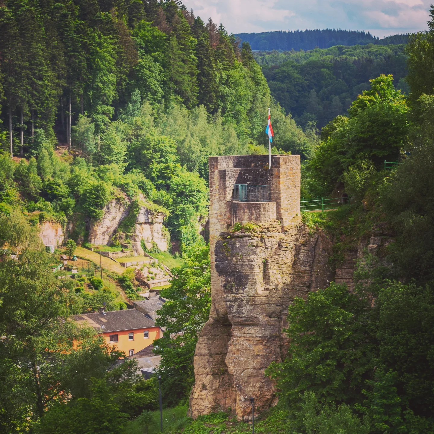 A stone tower flying the Luxembourg flag, perched on a rocky outcrop.