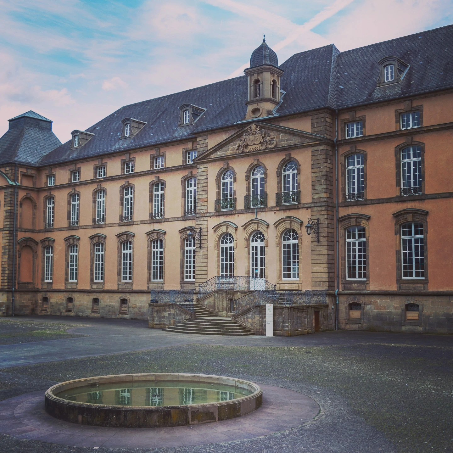 Grand historic building with tall windows and a small fountain in the courtyard of Echternach Abbey.