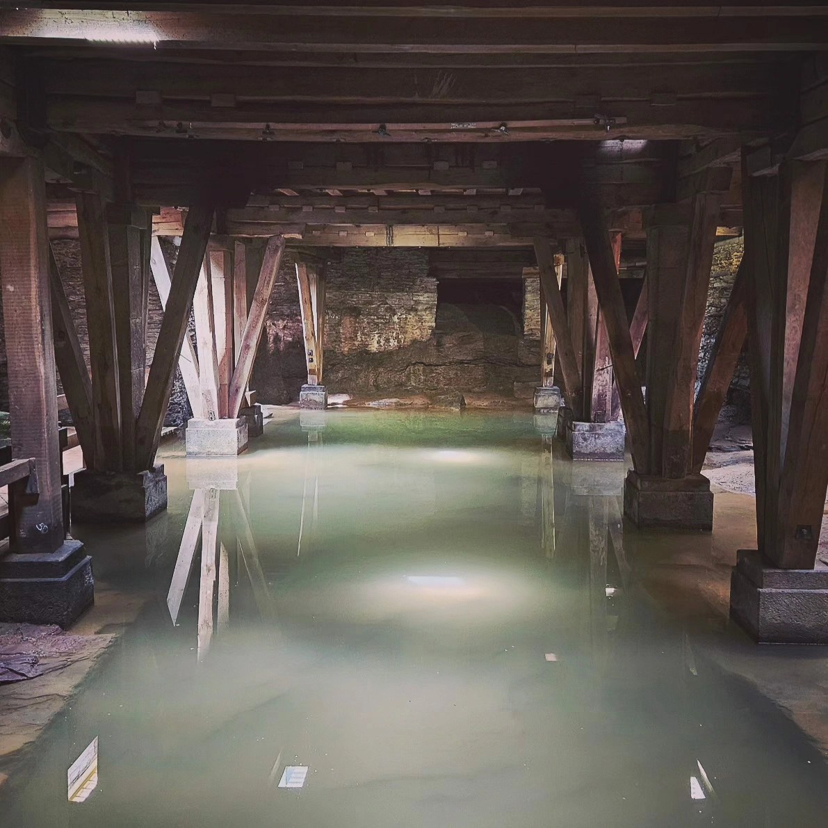 Chamber beneath Trier’s Roman amphitheater with wooden beams and still water on the floor.