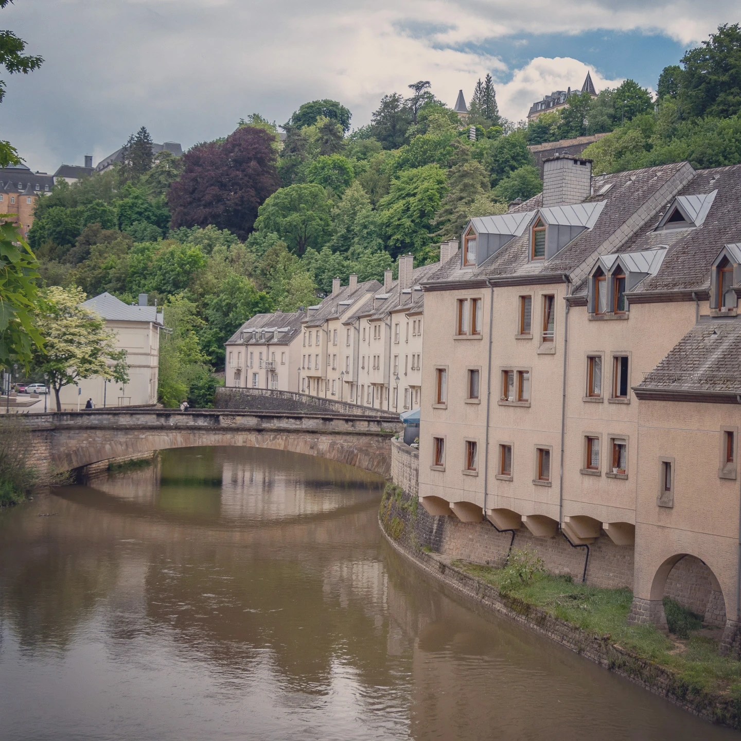 Row of pastel houses along the Alzette River with a stone bridge in Luxembourg City.