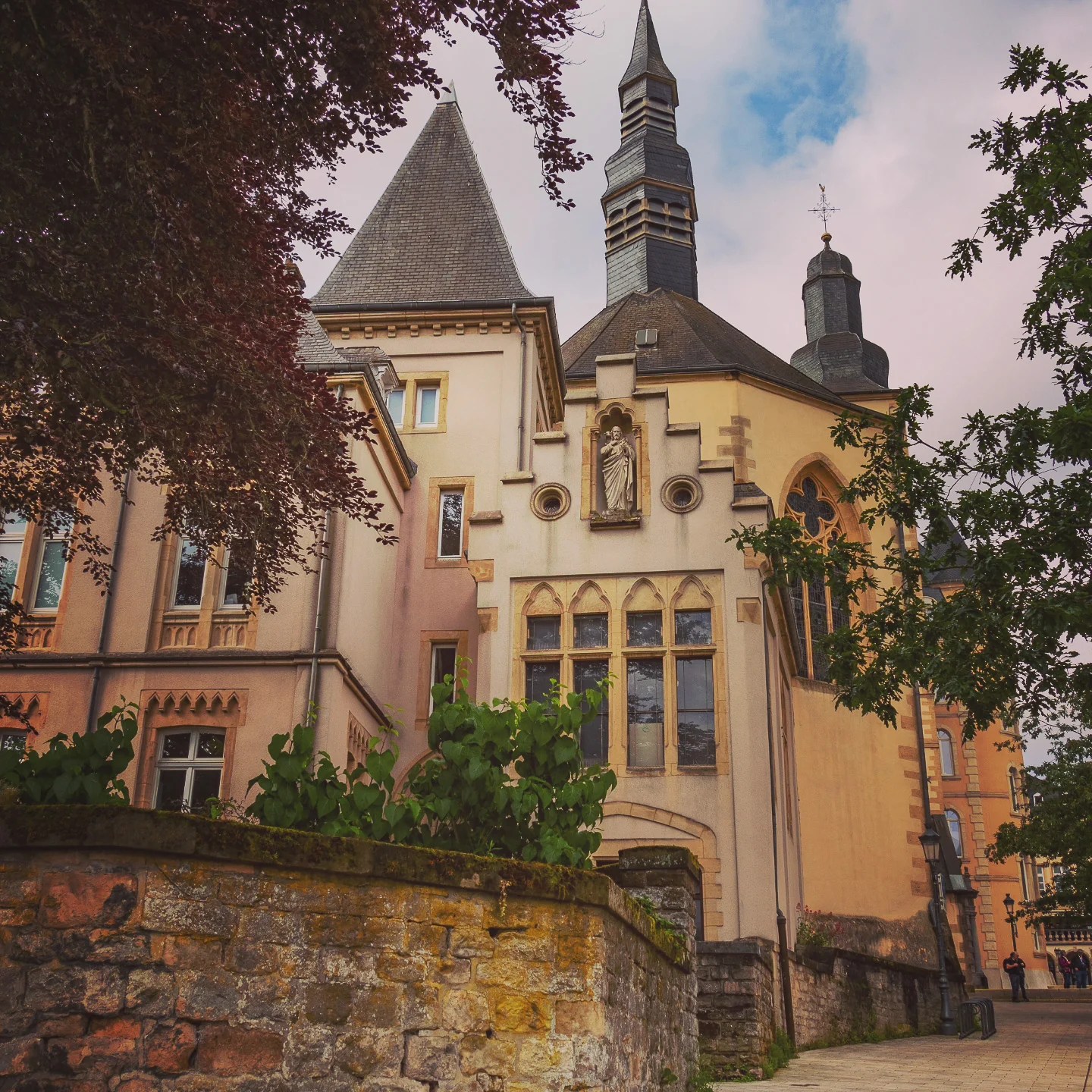 Church building with Gothic windows, spires, and statue niche in Luxembourg City.