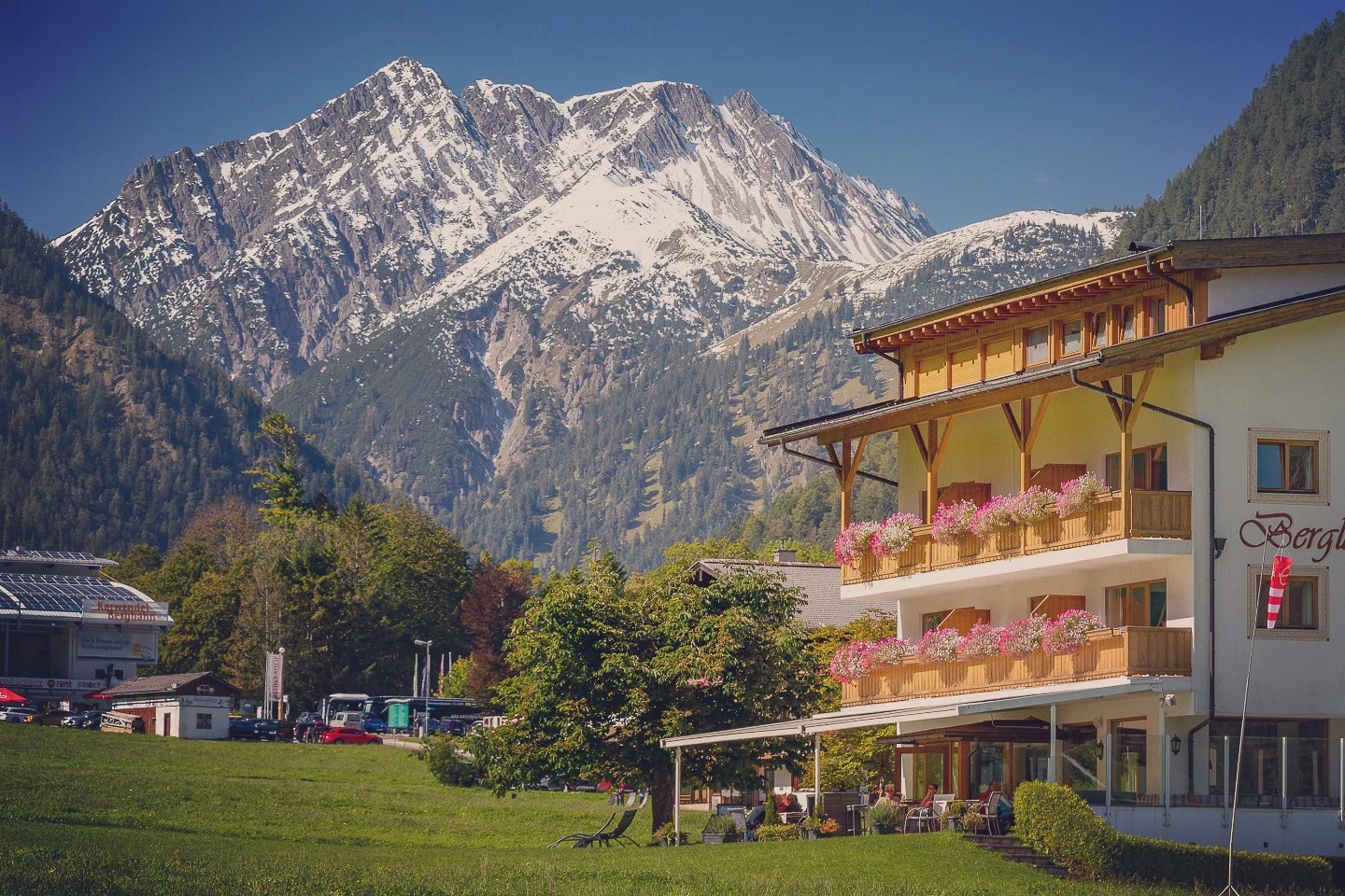 Alpine hotel with flower-filled balconies beneath snowcapped Karwendel peaks in Pertisau am Achensee, Tyrol.