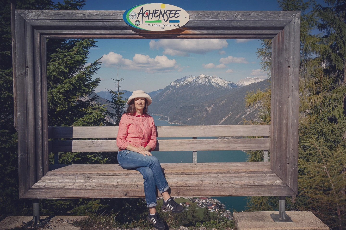 Traveler seated on an oversized wooden frame bench overlooking Achensee and snowy peaks.