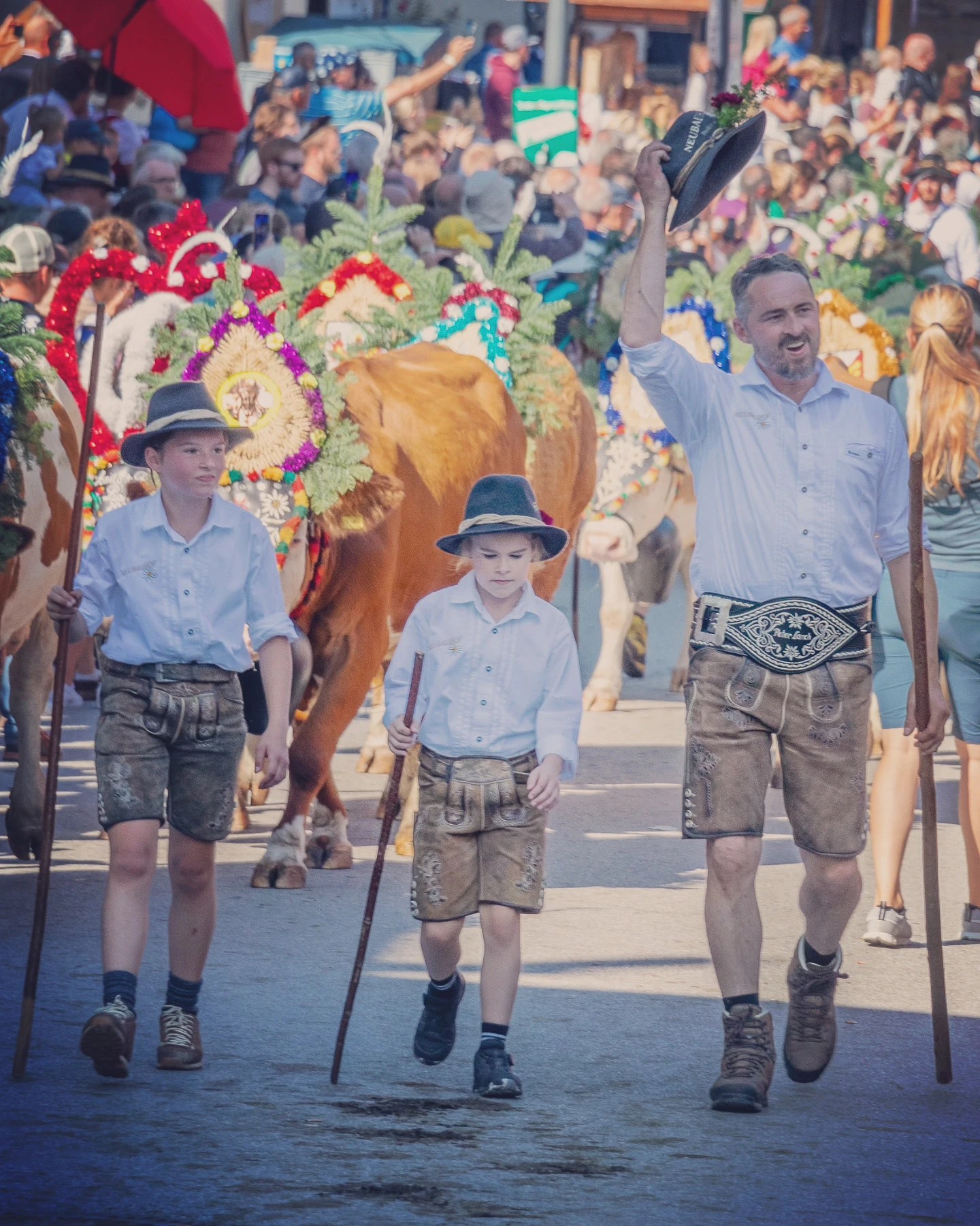 Herders in lederhosen lead flower-crowned cows through Reith im Alpbachtal during the Almabtrieb parade; one tips his hat to the crowd.