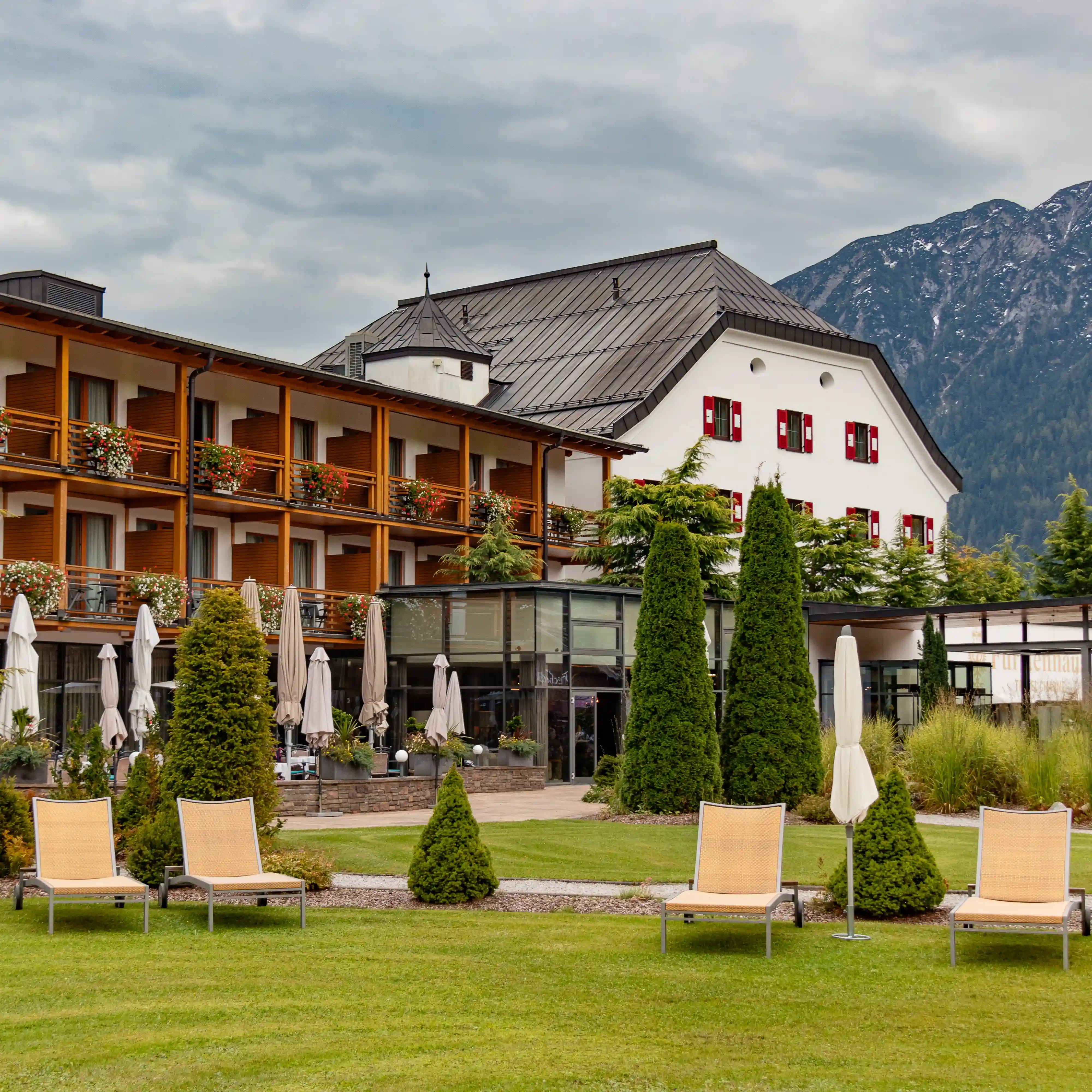 Travel Charme Fürstenhaus Achensee in Pertisau with red window shutters, a wooden wing, manicured lawns, and mountain backdrop.