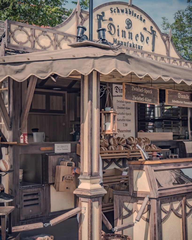 A wood-framed food stall labeled “Schwäbische Dinnede Manufaktur,” selling traditional flatbreads and rustic loaves.