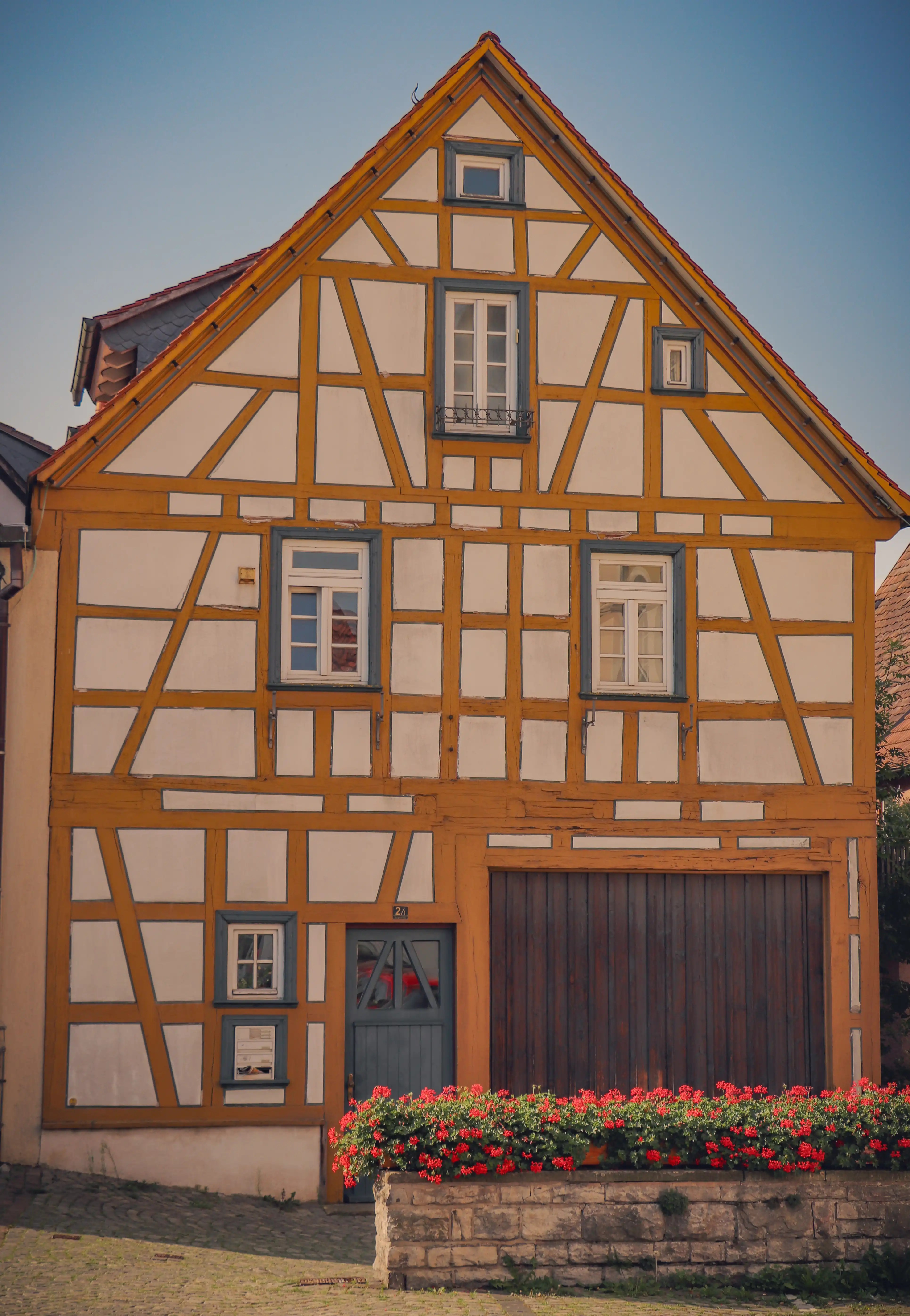 Mustard-and-white half-timbered house with blue-gray windows and a bed of red geraniums, Bad Wimpfen old town.