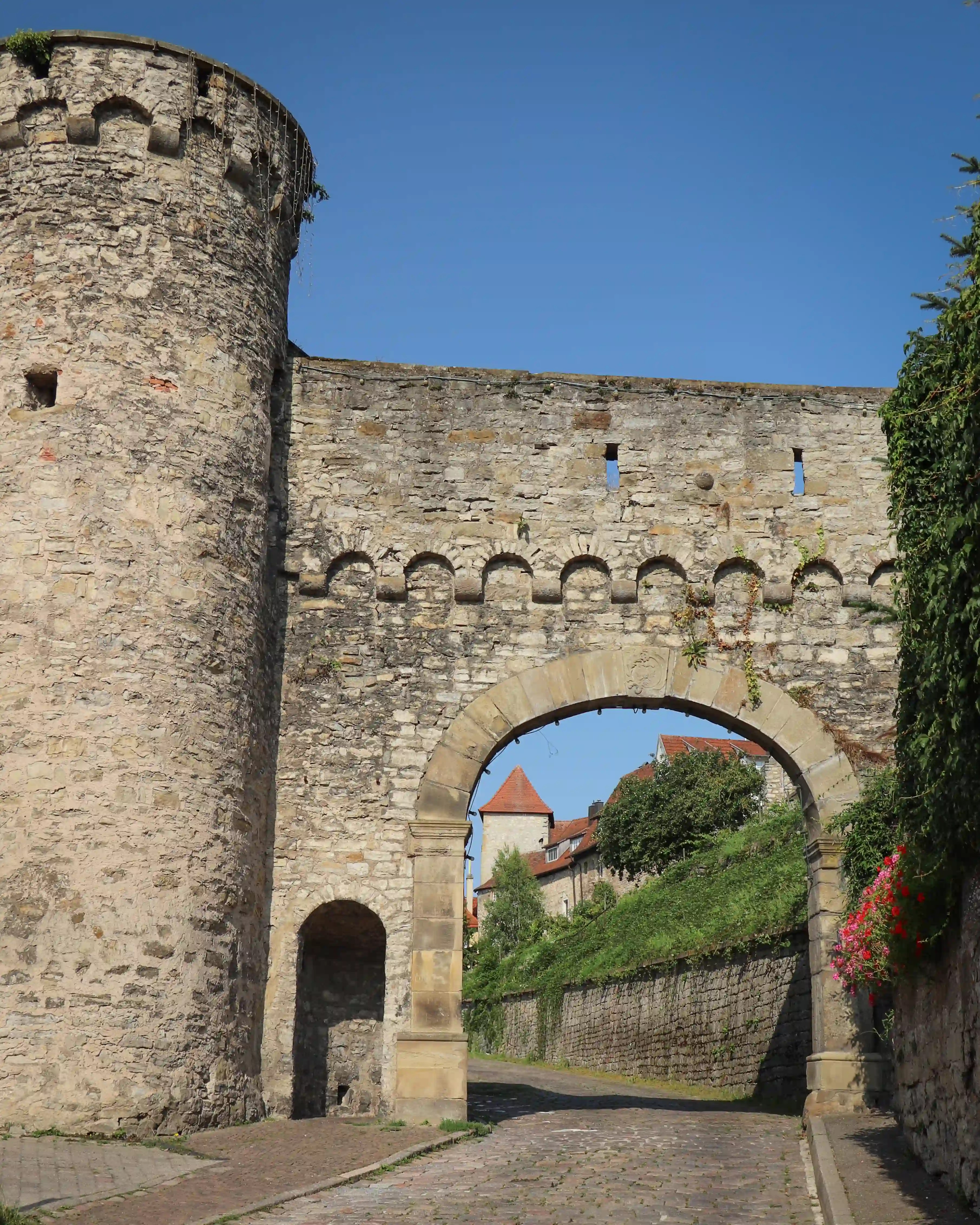 Stone city gate with crenellations and a wide arch over a cobbled road, Bad Wimpfen, Germany.