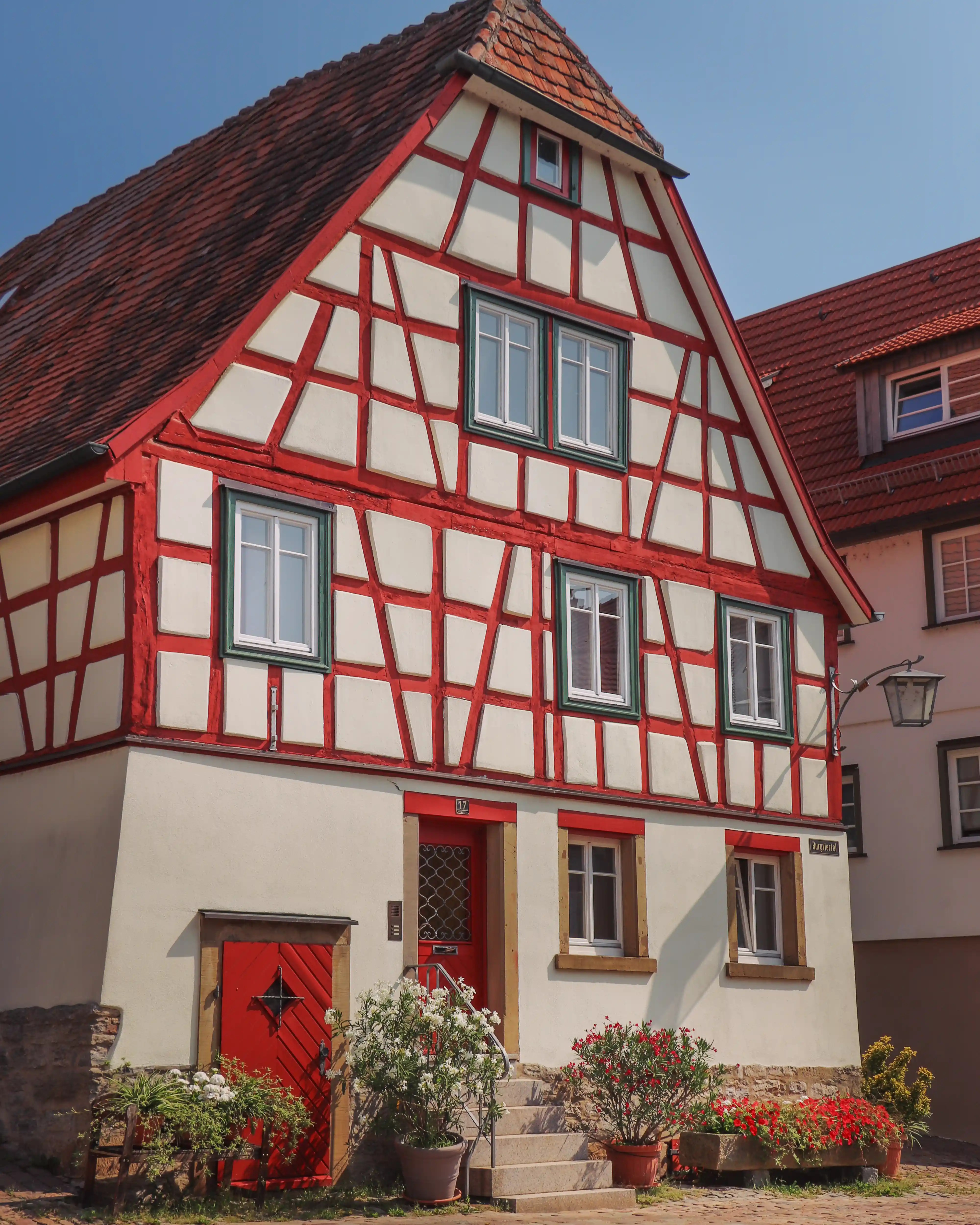 Red-framed half-timbered house with green-trimmed windows and potted flowers, Bad Wimpfen.