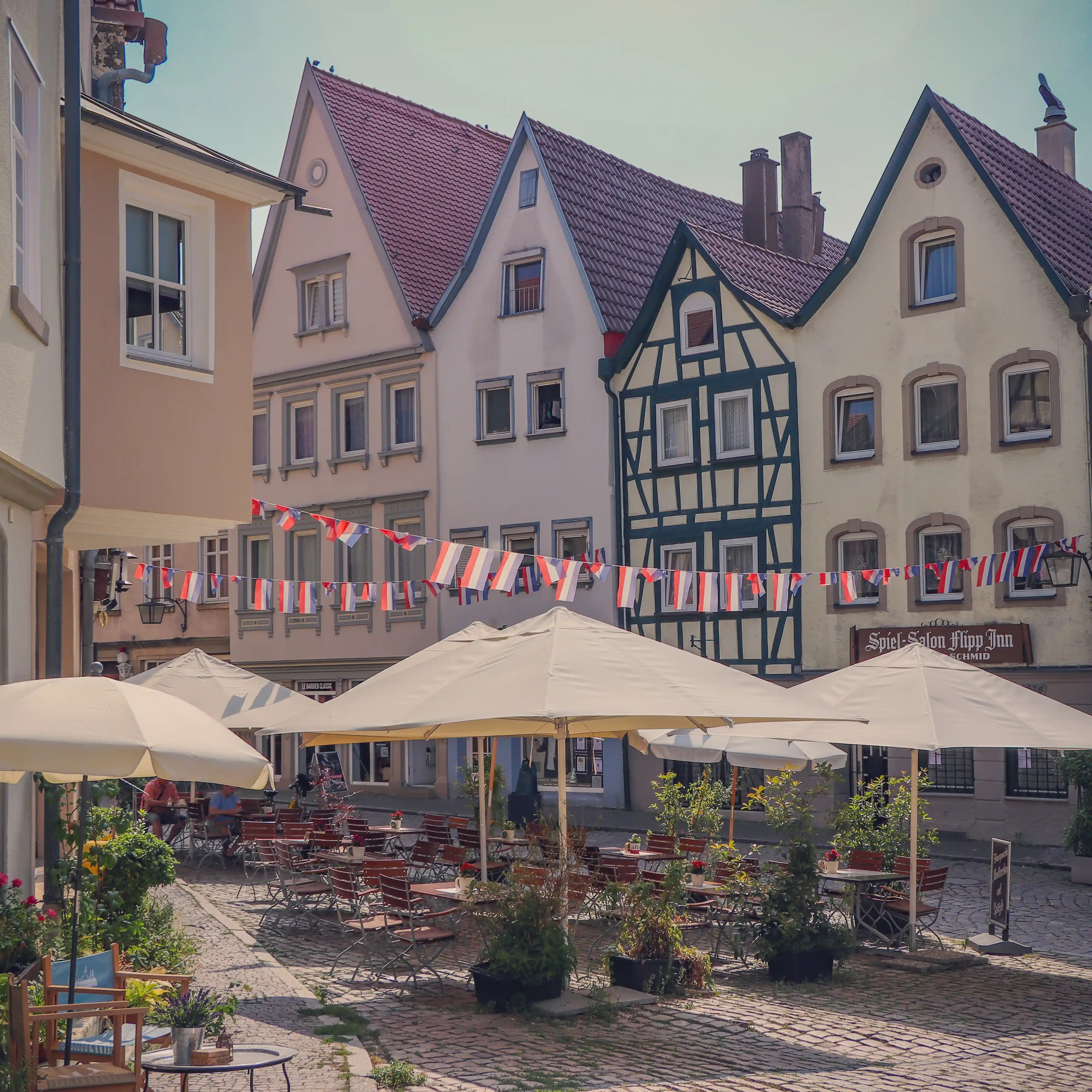 Café terrace with umbrellas and bunting on a cobbled square lined with gabled and half-timbered houses, Bad Wimpfen.