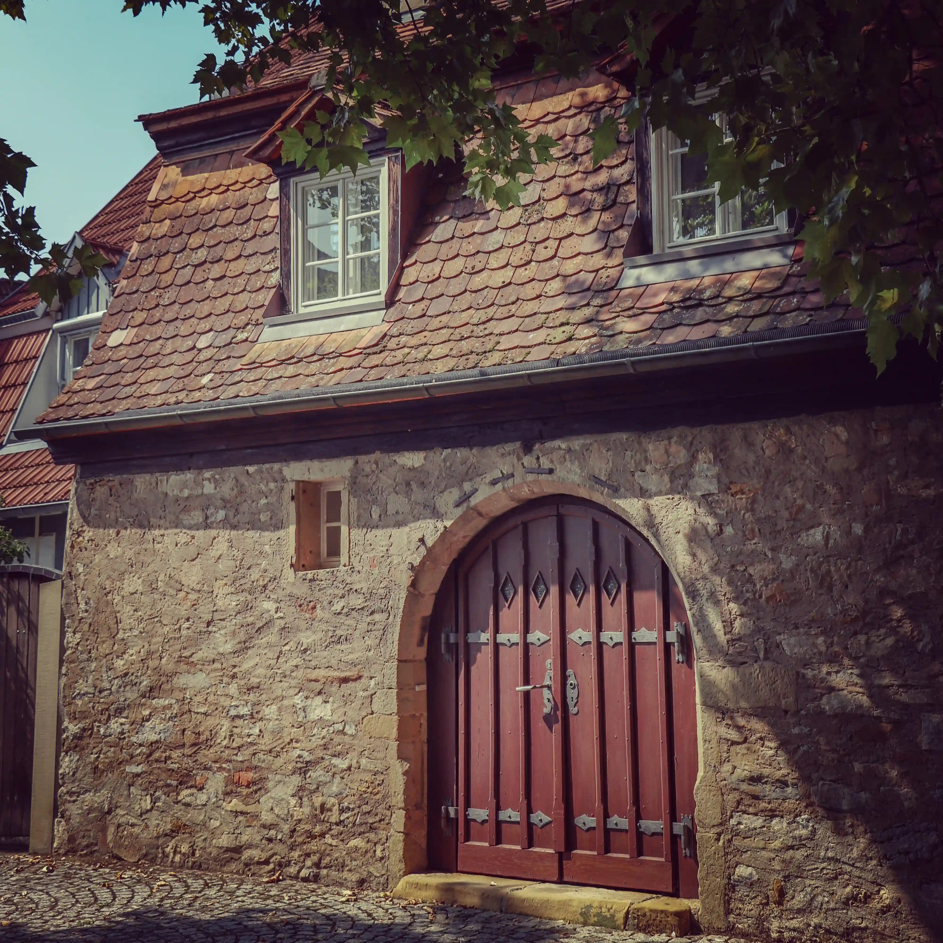 Stone cottage with a red arched wooden door under leafy shade, Bad Wimpfen.