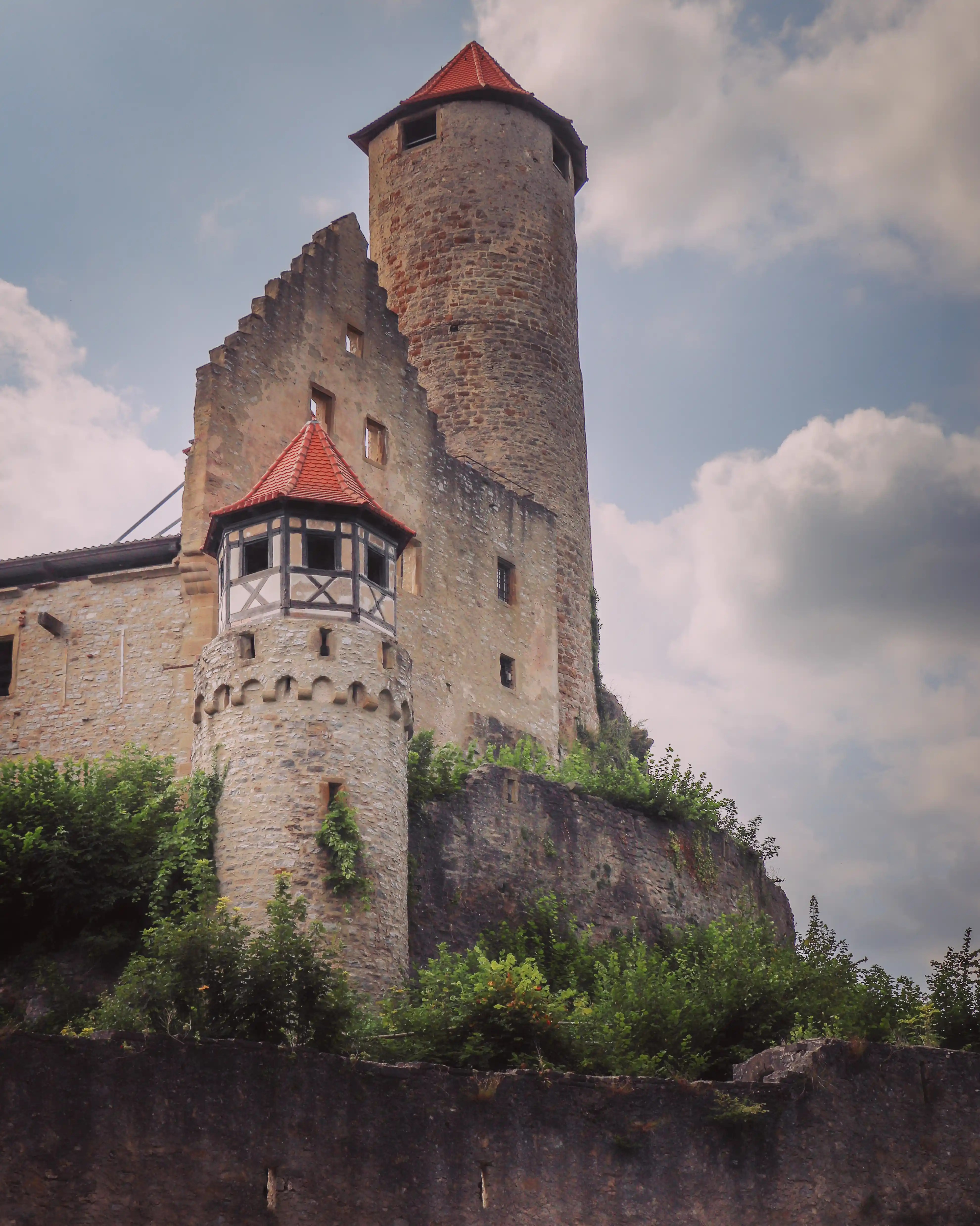 Close view of Burg Hornberg’s round tower and keep with red roofs and half-timbered lookout on a cliff.