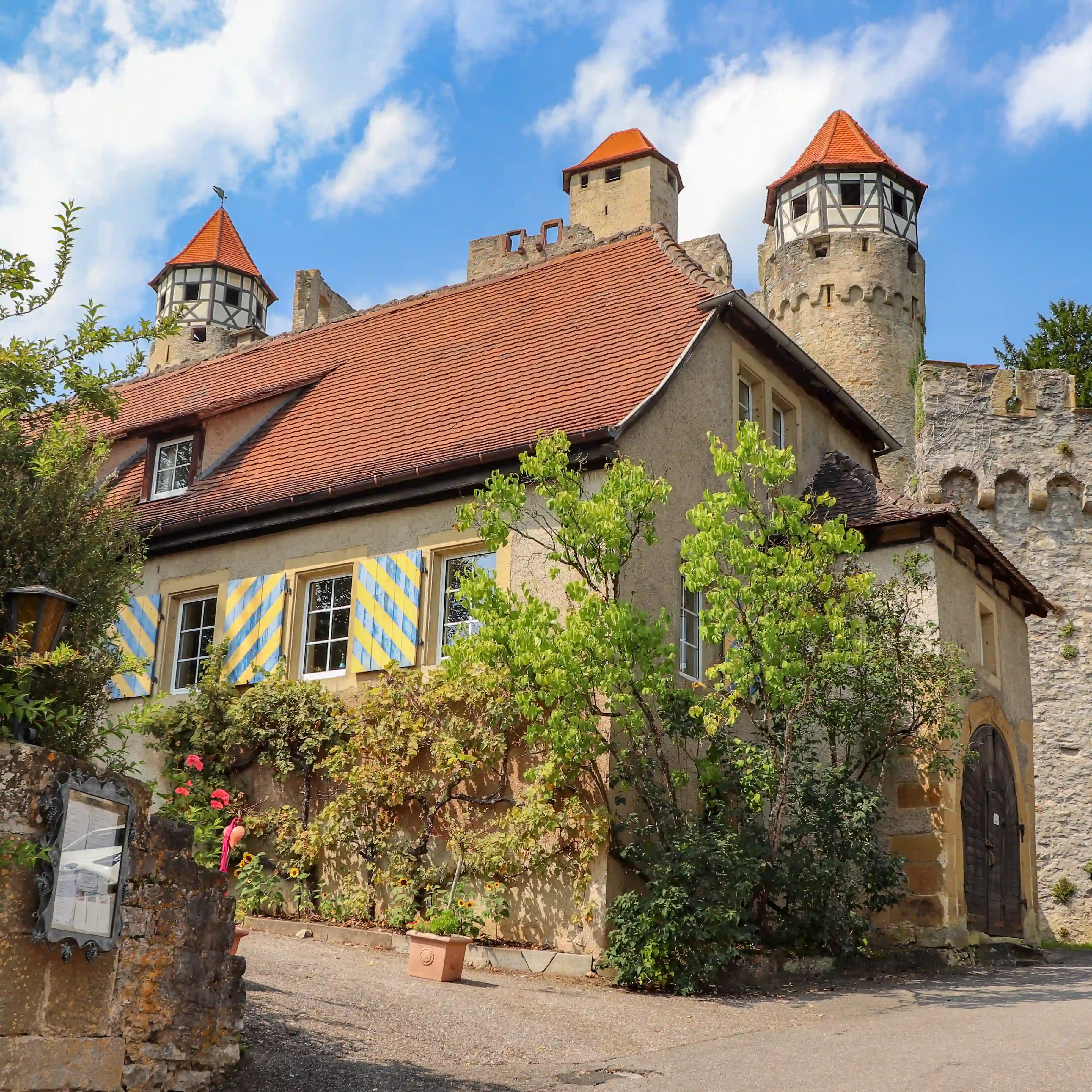 Stone building with blue-and-yellow shutters inside Burg Hornberg, towers of the castle behind.