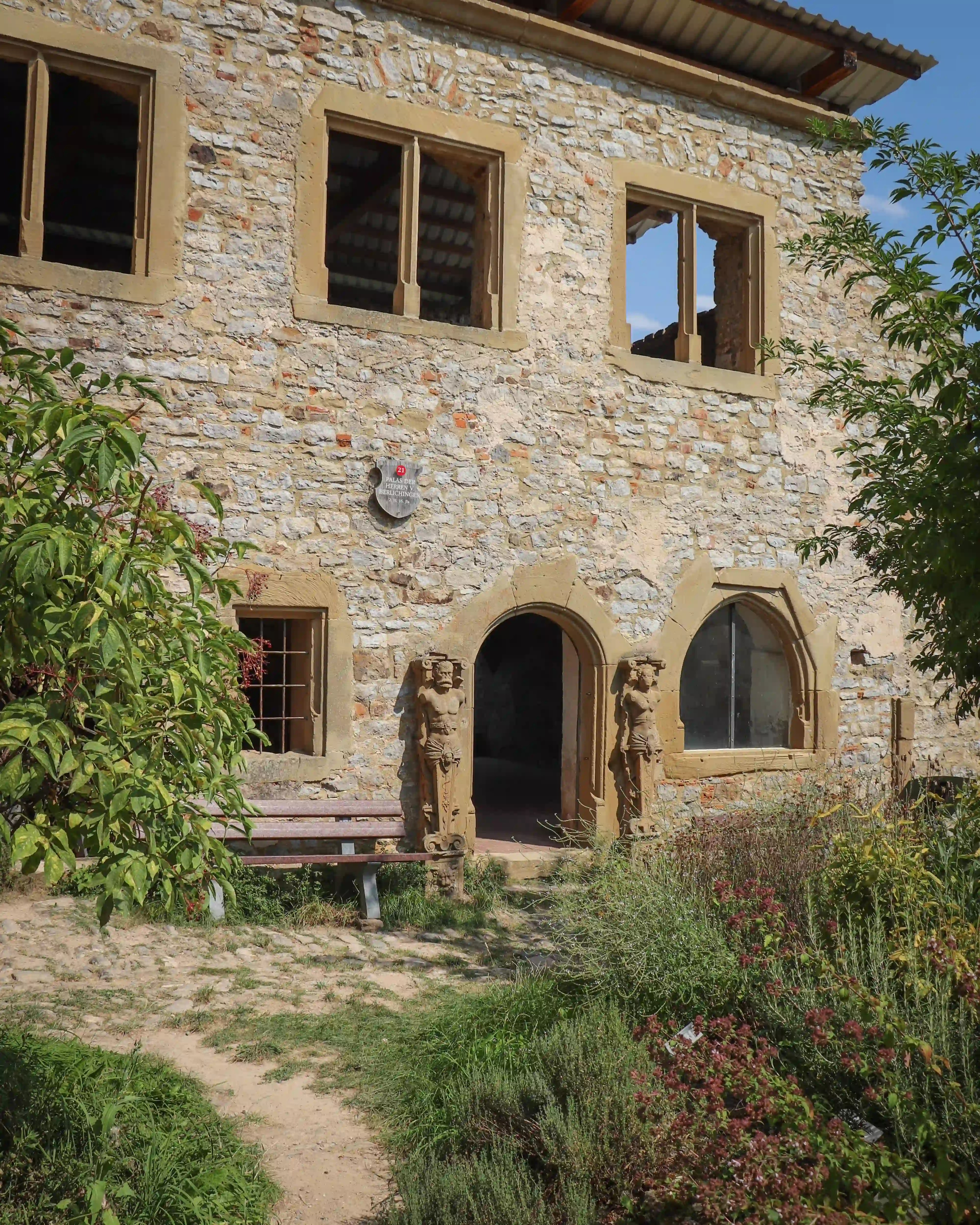 Garden path to a stone building at Burg Hornberg with two atlantes figures framing the arched door.