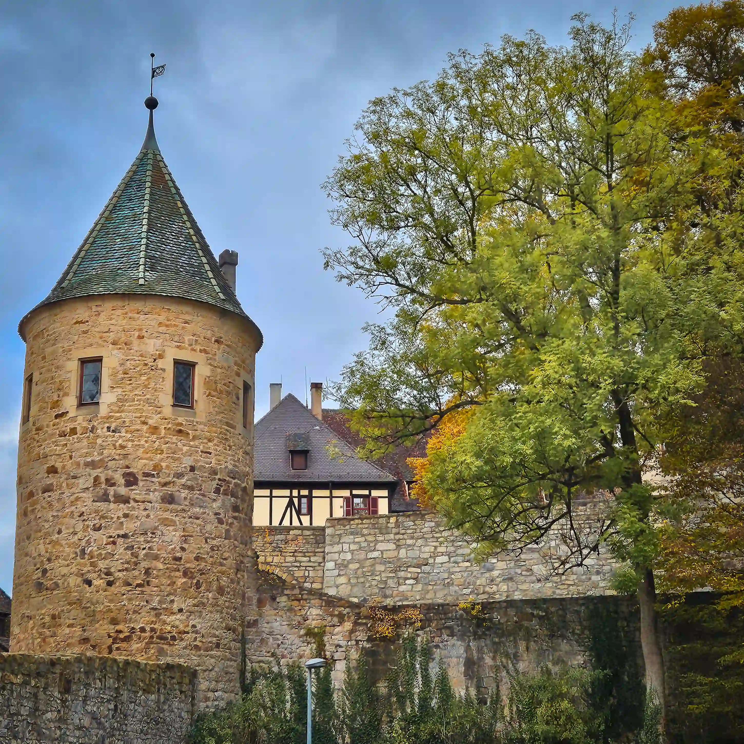Round medieval watchtower and stone wall at Kloster und Schloss Bebenhausen with autumn trees.