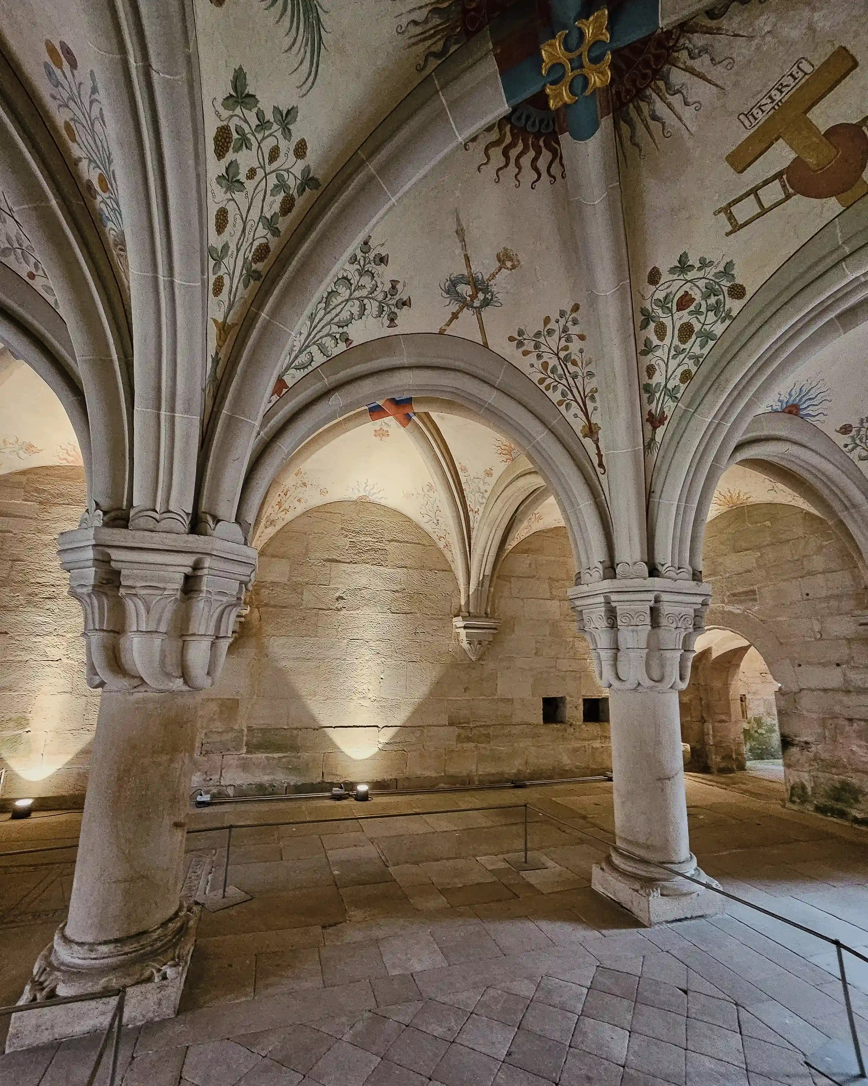 Gothic vaulted hall at Bebenhausen with painted ceilings featuring plants, tools, and symbolic designs.