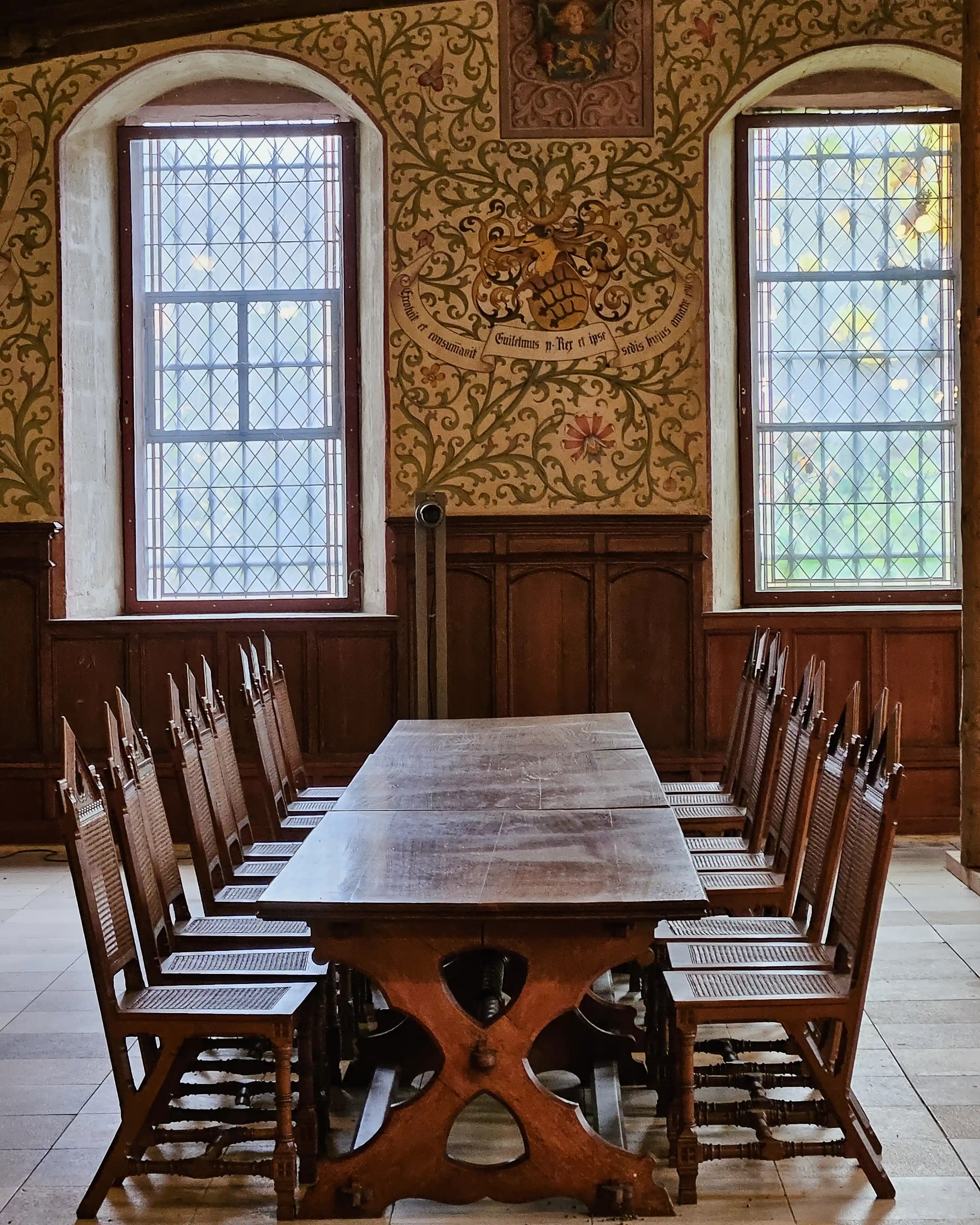 Wooden dining table and chairs in Bebenhausen with painted walls and glass windows.