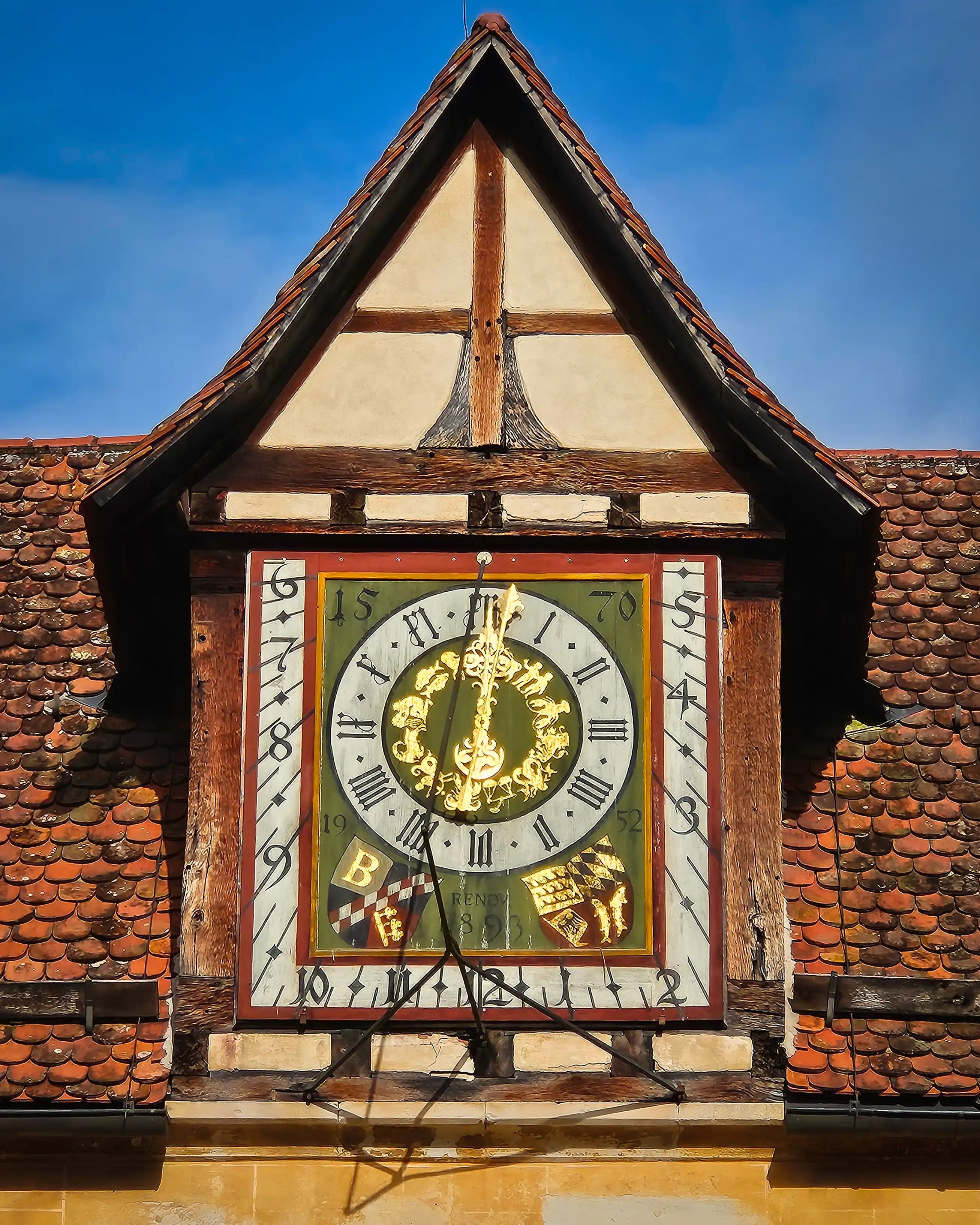 Historic clock face with Roman numerals and golden decorations on the roofline at Bebenhausen.