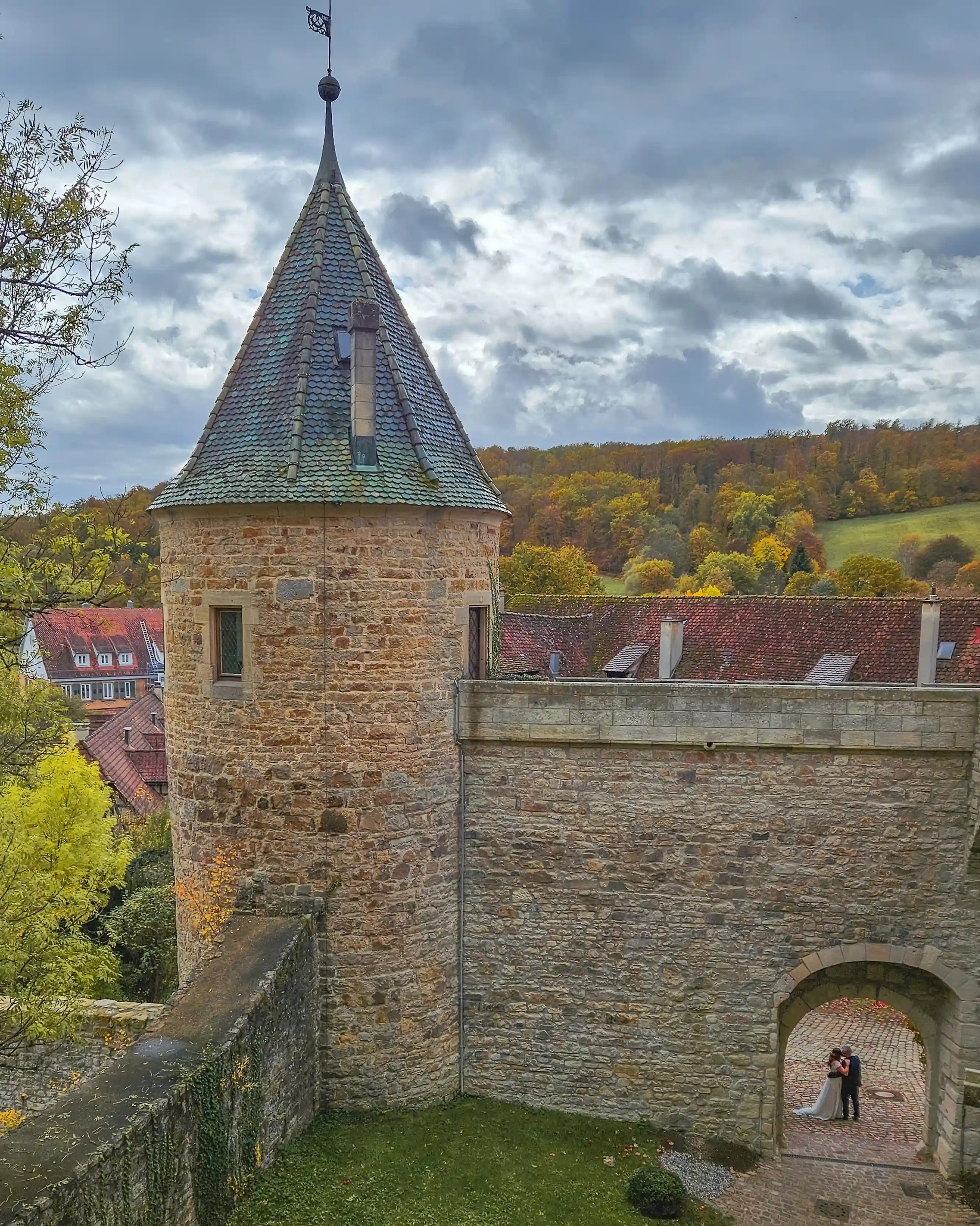 Round medieval watchtower with pointed roof and a bride and groom standing in the arched gate at Bebenhausen.