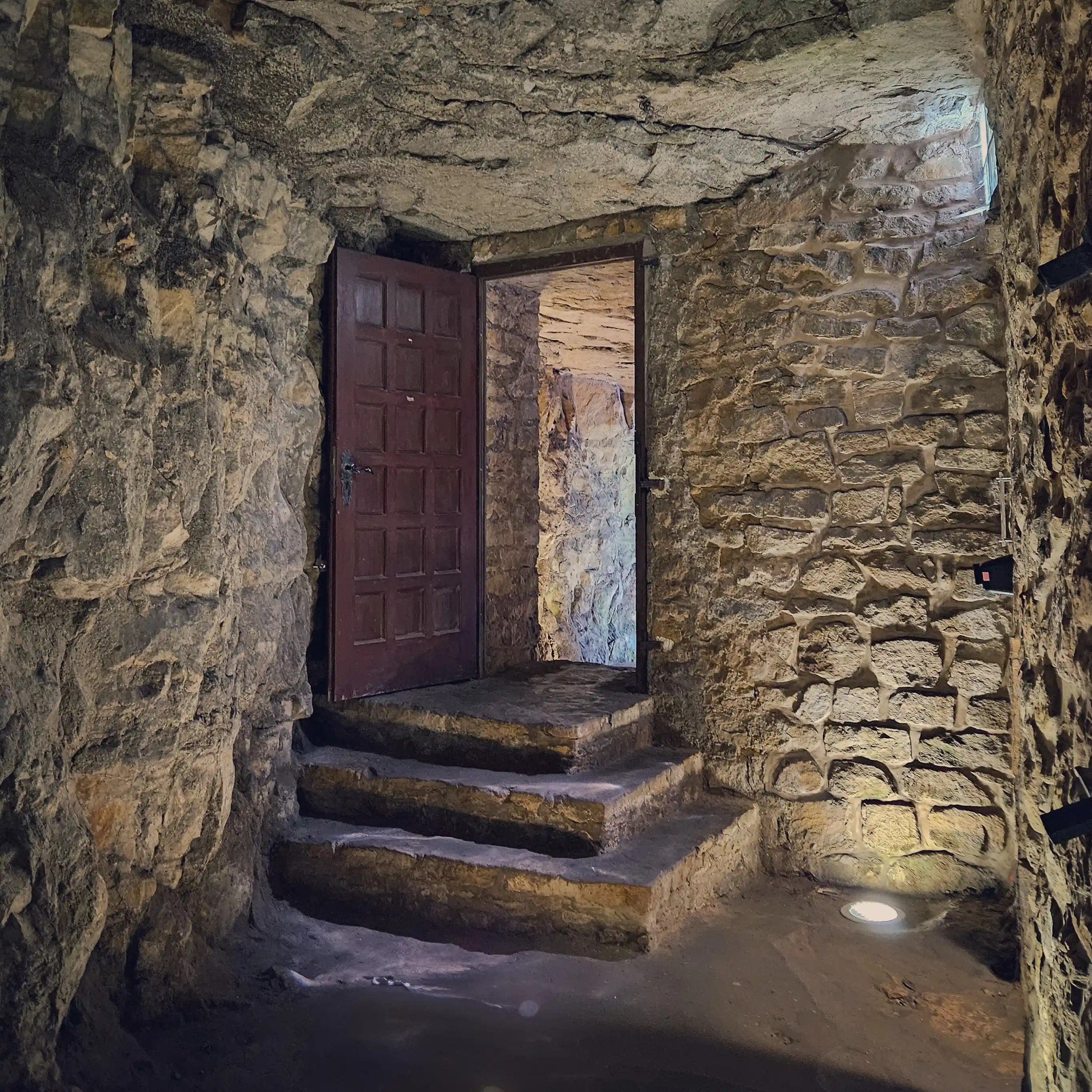 A stone-walled passage inside Luxembourg’s casemates, featuring steps leading to a heavy wooden door.