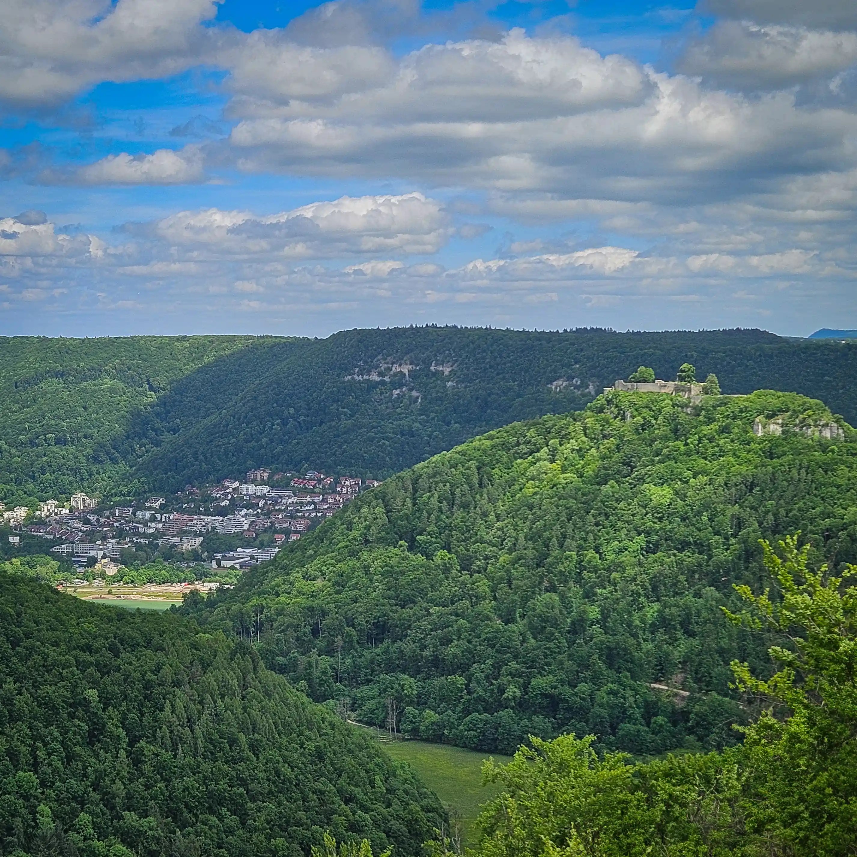 View across forested hills toward Hohenurach Castle ruins with the town of Bad Urach visible in the valley below.