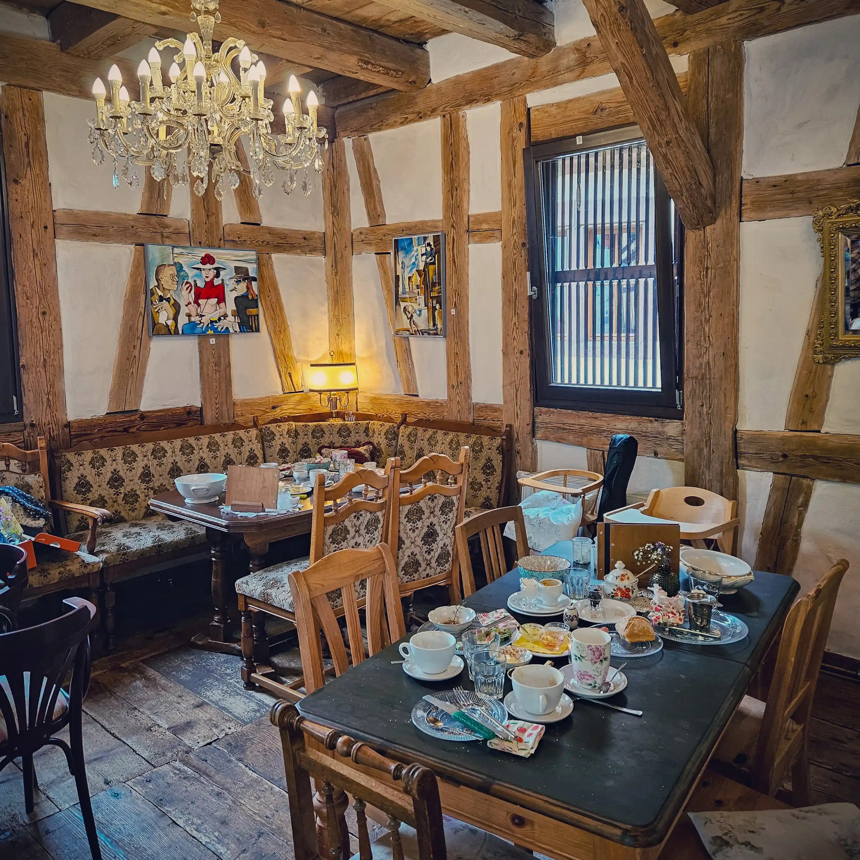 Cozy interior of Café im Kloster in Hirsau Monastery with timber-framed walls, chandelier, and tables set with teacups and plates.