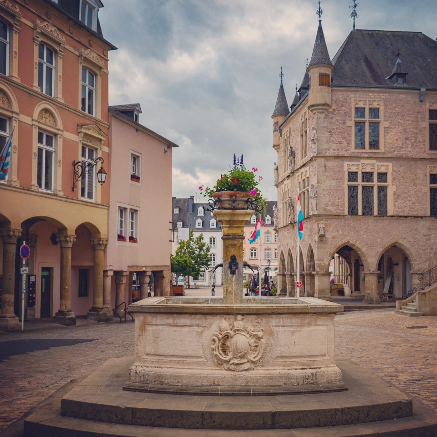 Stone fountain with a flower planter in Echternach’s medieval square, surrounded by historic buildings.
