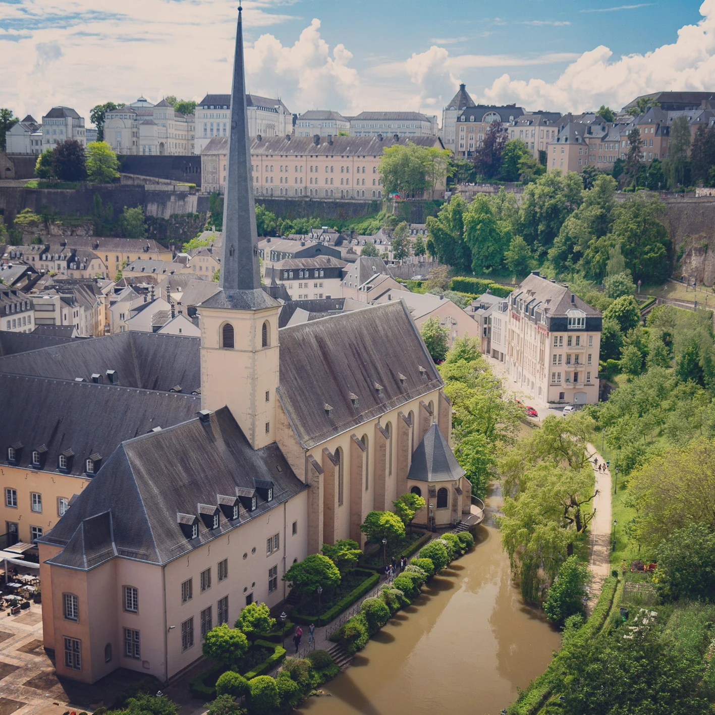 Neumünster Abbey with tall spire along the Alzette River in Luxembourg’s Grund.