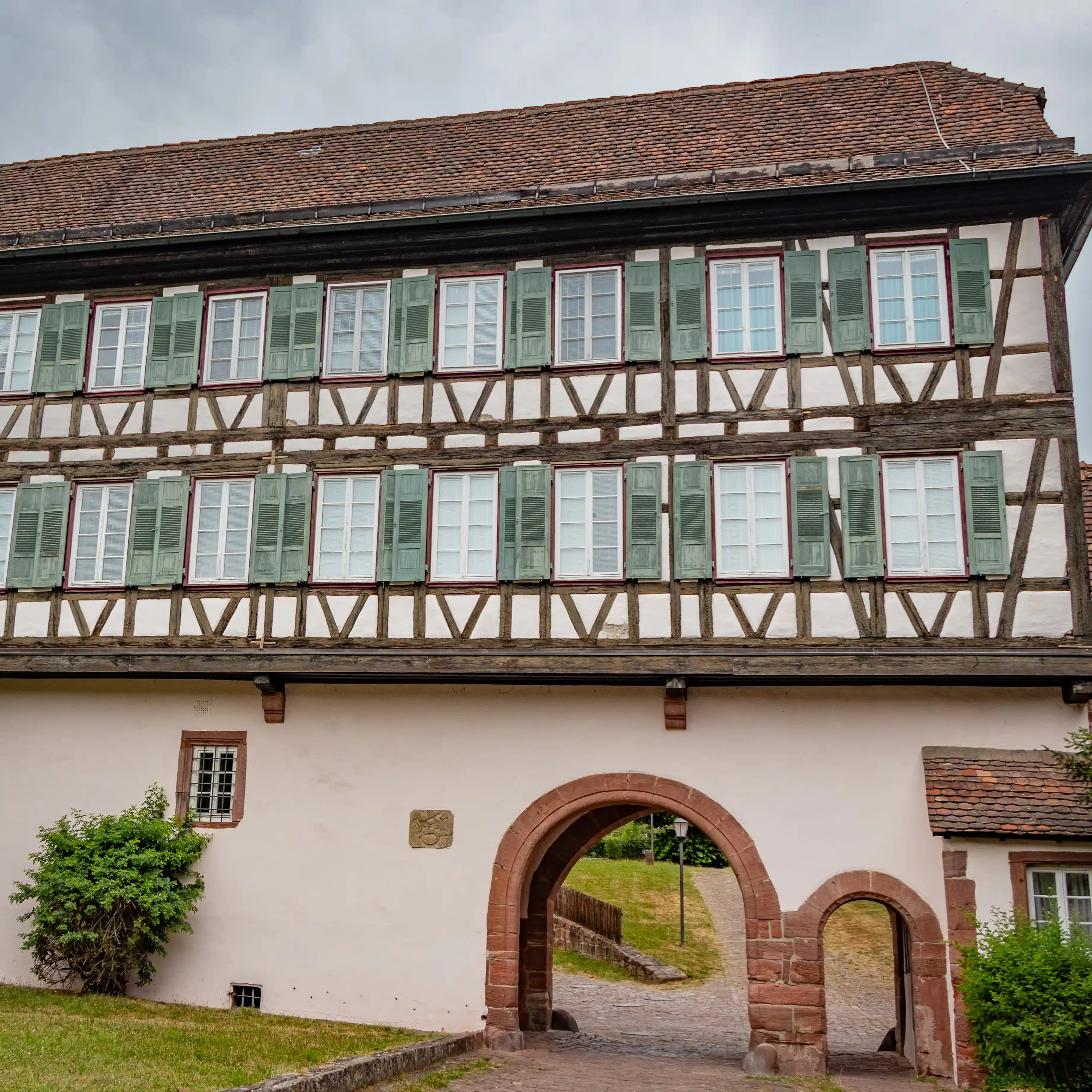 Half-timbered gatehouse at Hirsau Monastery with green shutters and arched stone entrance.