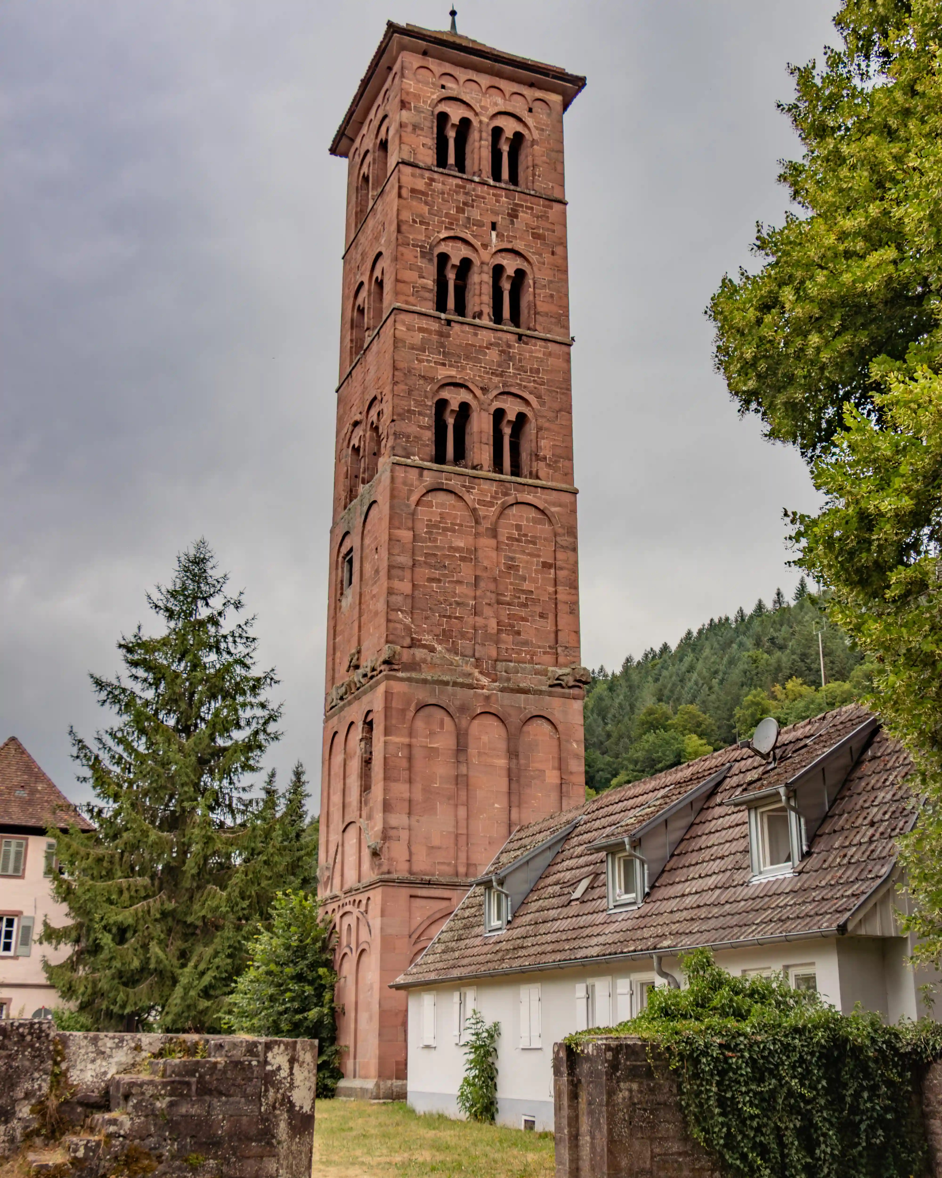 Tall Romanesque tower of Hirsau Monastery rising above trees and nearby houses.
