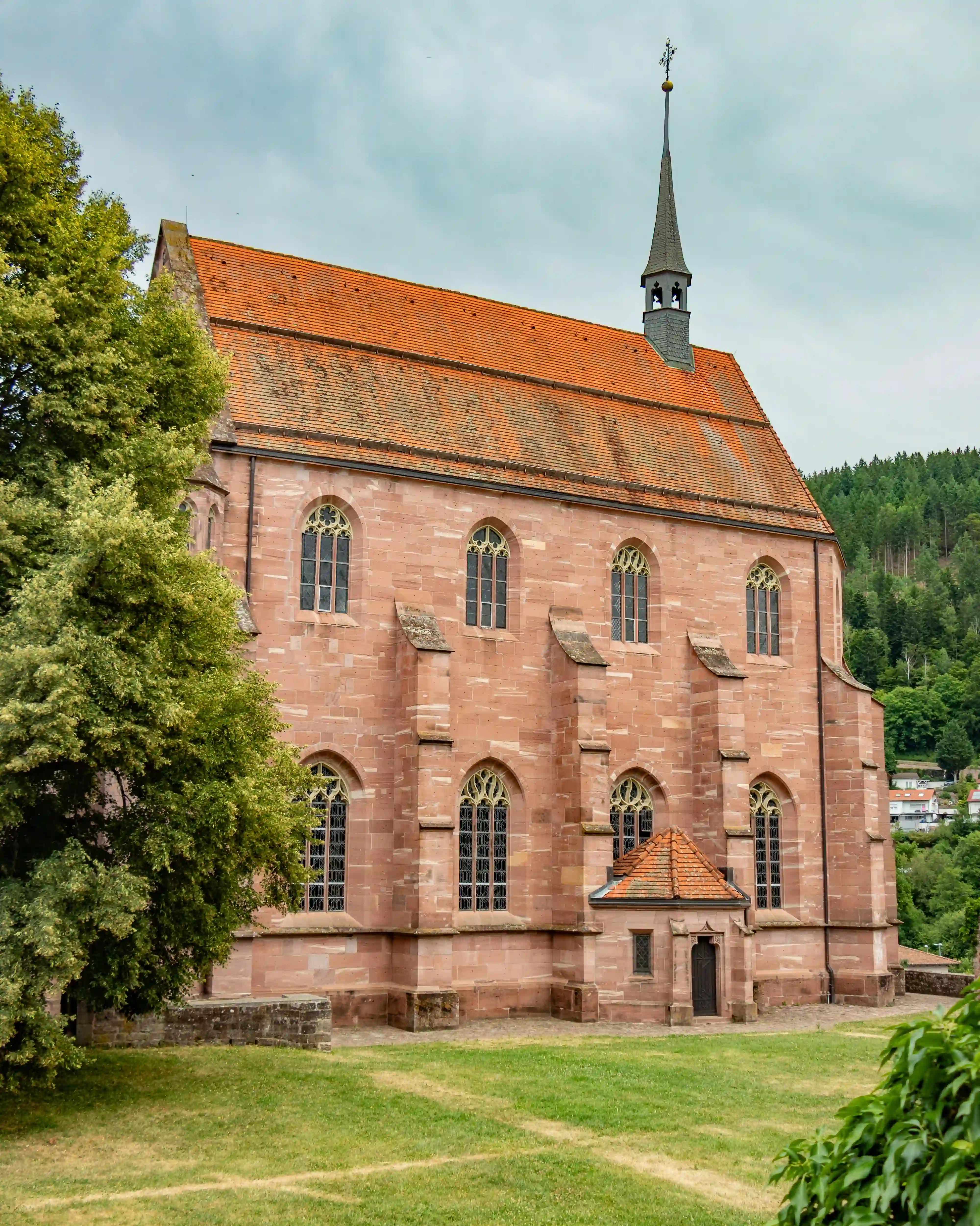 Side view of the red sandstone Chapel of St. Mary at Hirsau with stained-glass windows and tall steeple.