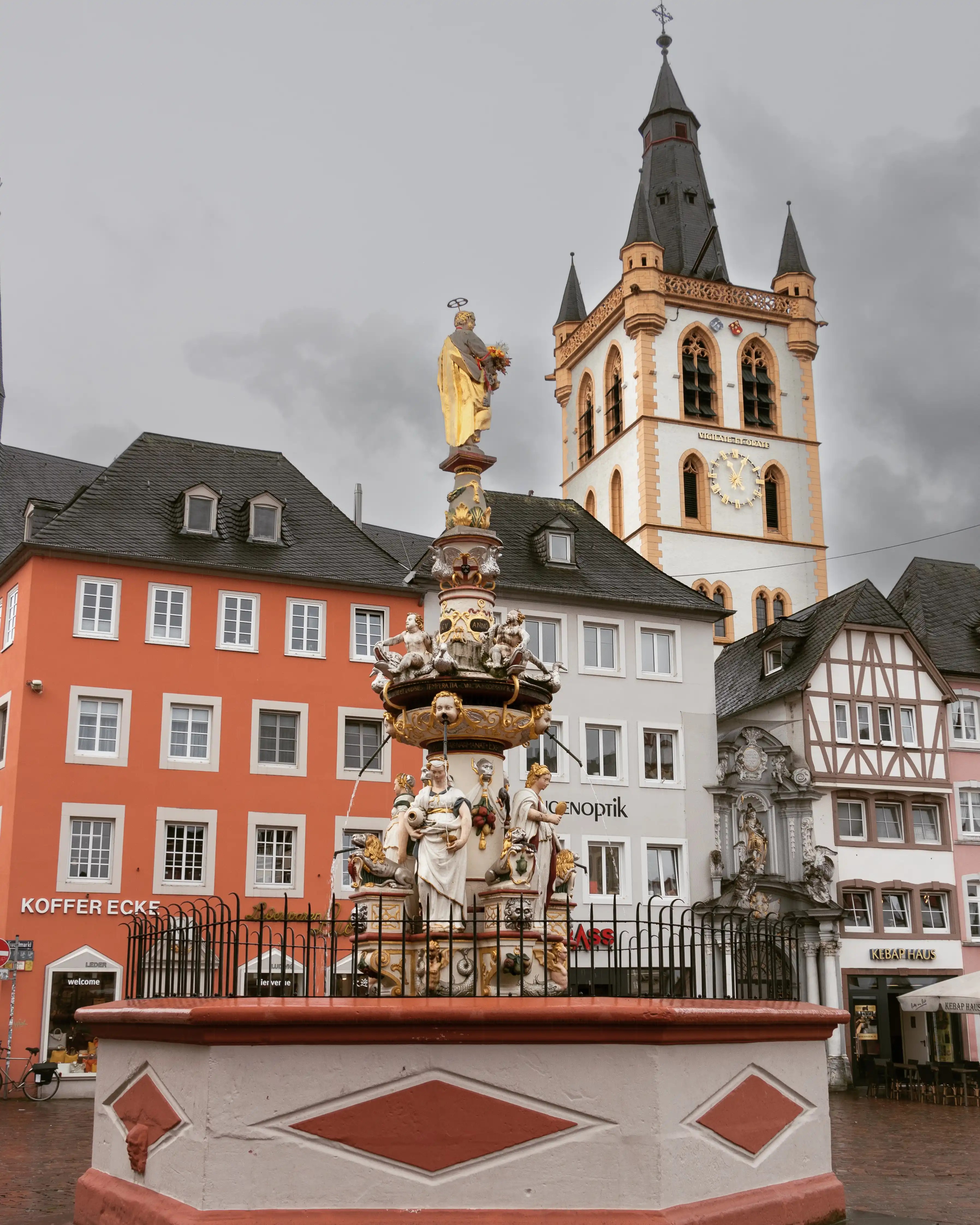 Ornate Renaissance fountain with golden statue in Trier’s Hauptmarkt, surrounded by historic buildings.