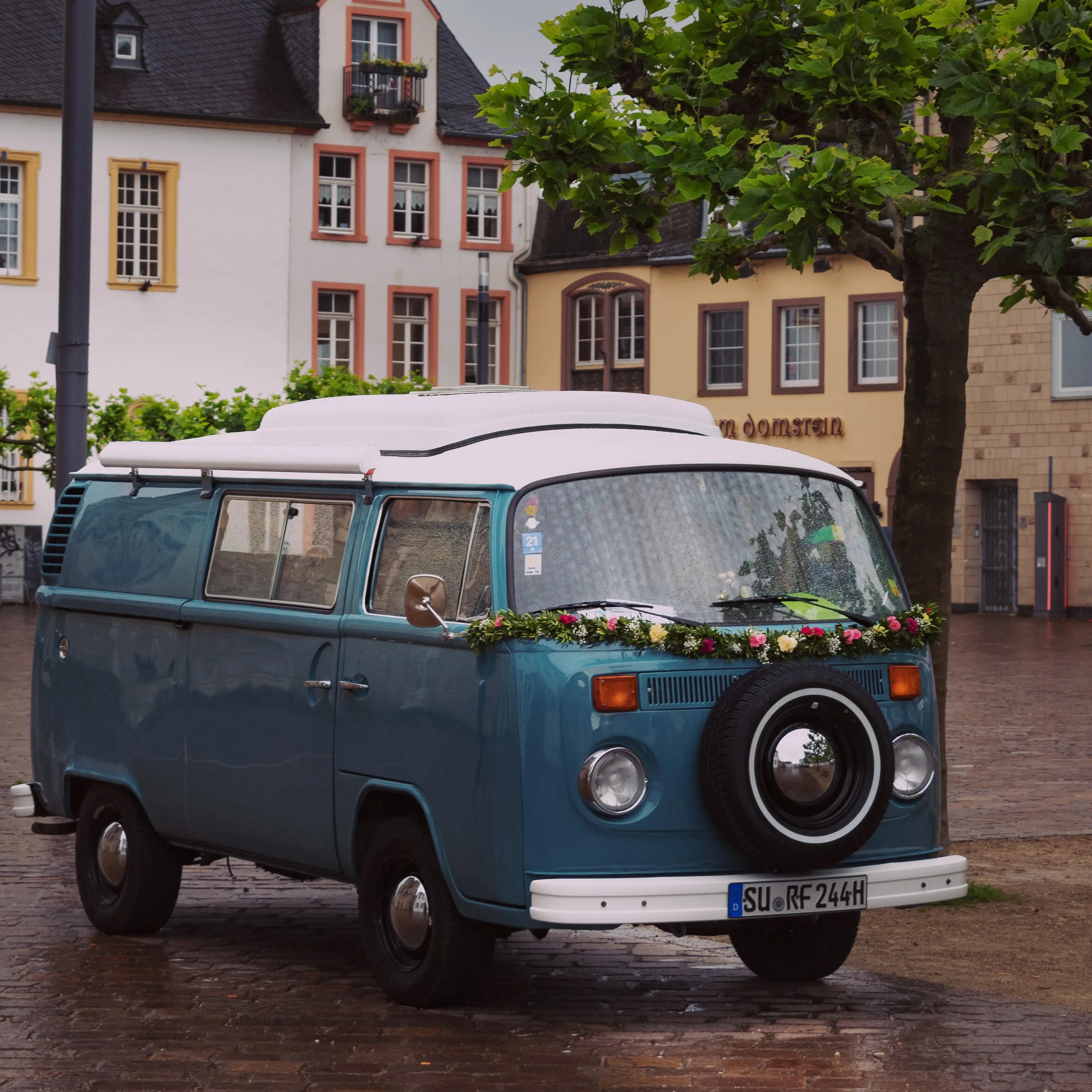 A blue vintage Volkswagen camper van decorated with flowers parked in Trier.