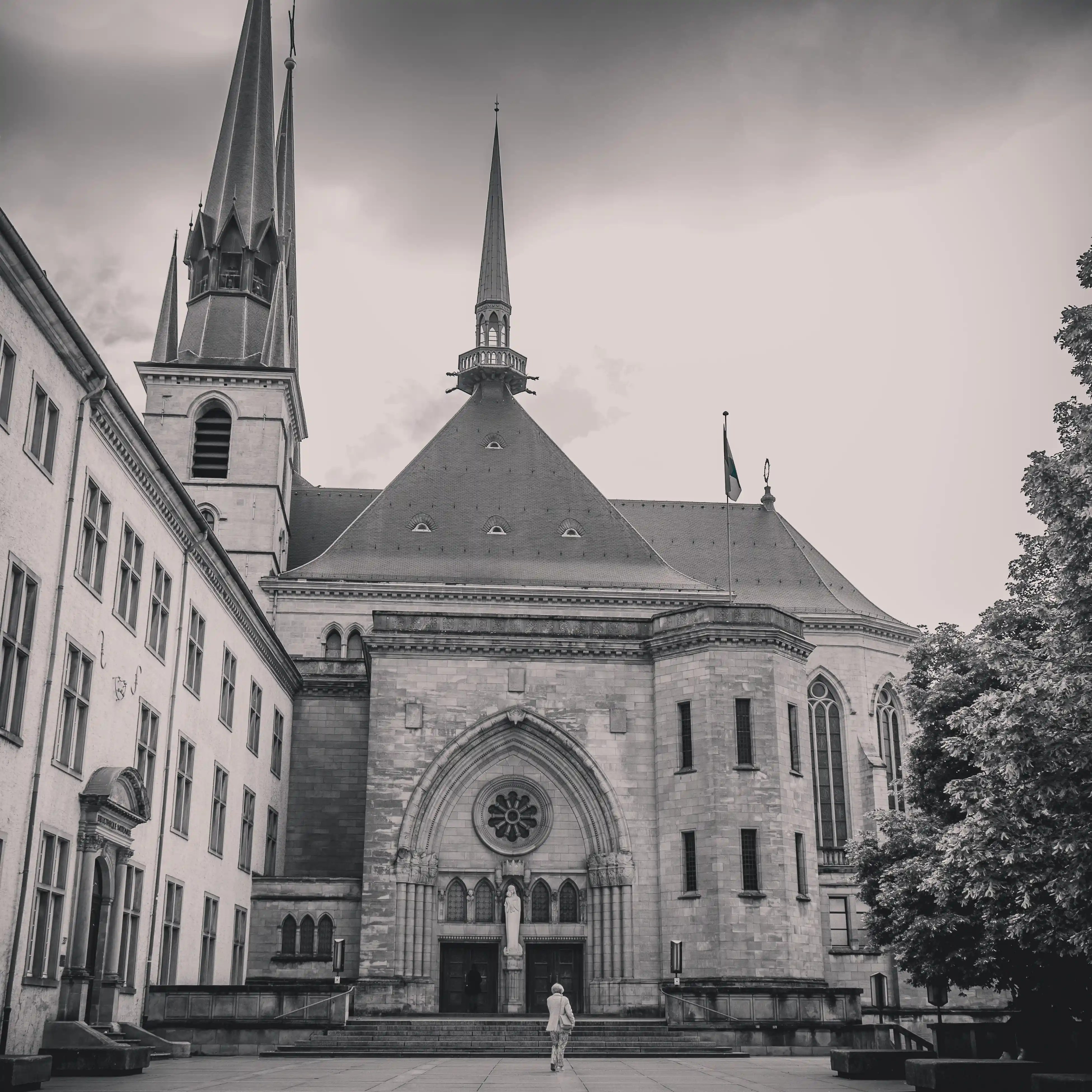 Black and white photo of the Notre-Dame Cathedral in Luxembourg, with its Gothic spires rising over the courtyard.