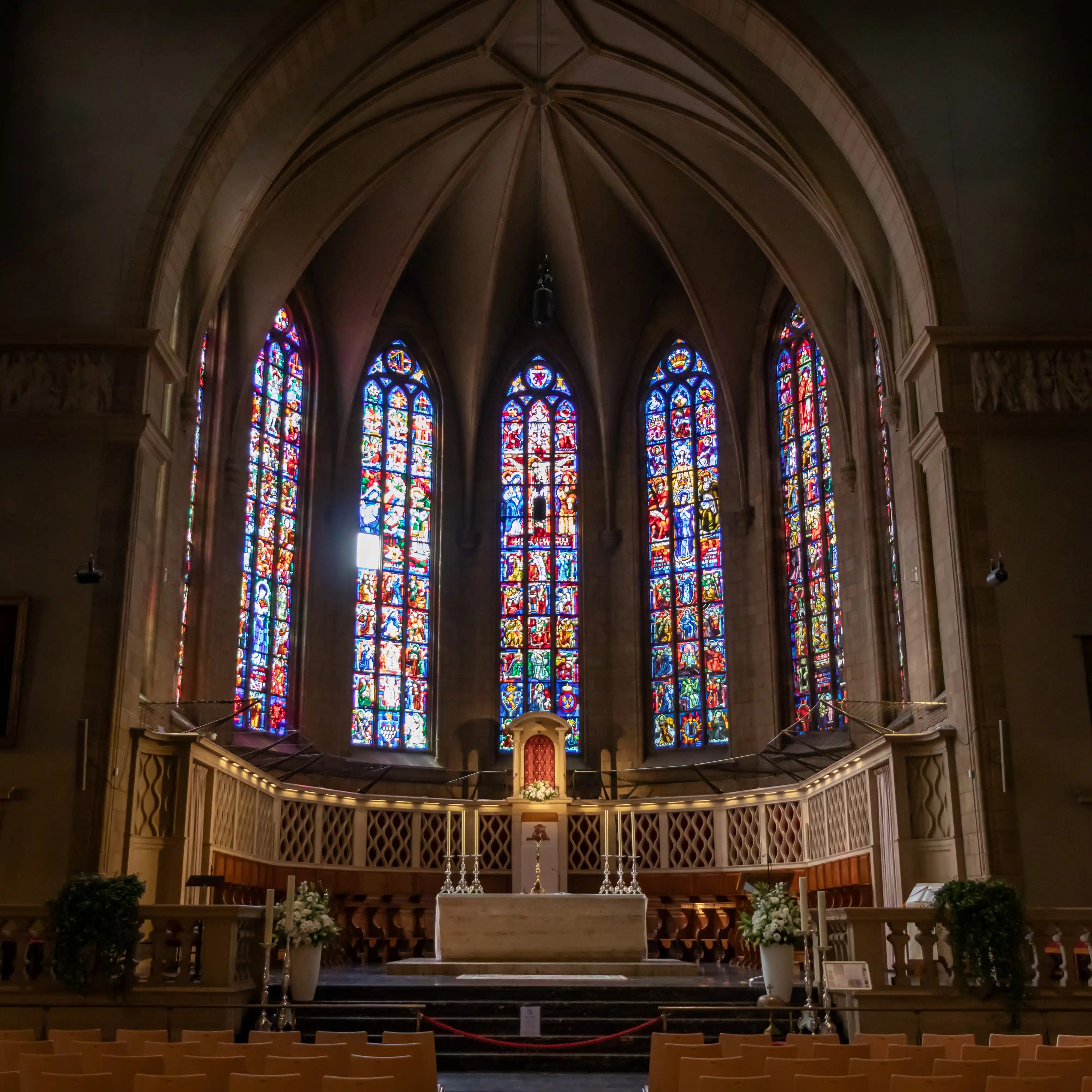 Interior view of the Notre-Dame Cathedral altar, with tall stained-glass windows in vivid colors behind it.