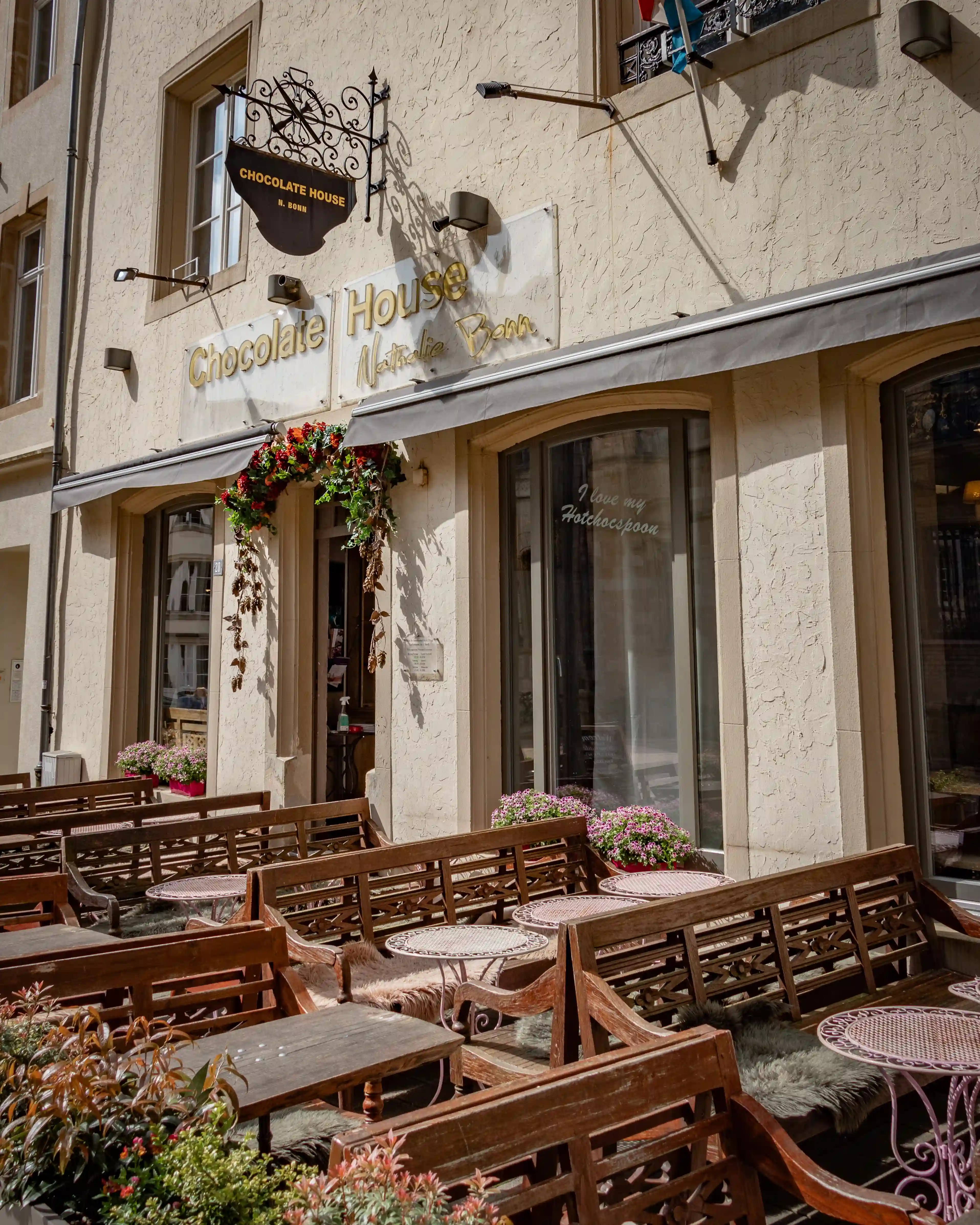 Outdoor seating area in front of the Chocolate House café, with wooden benches and flowers.