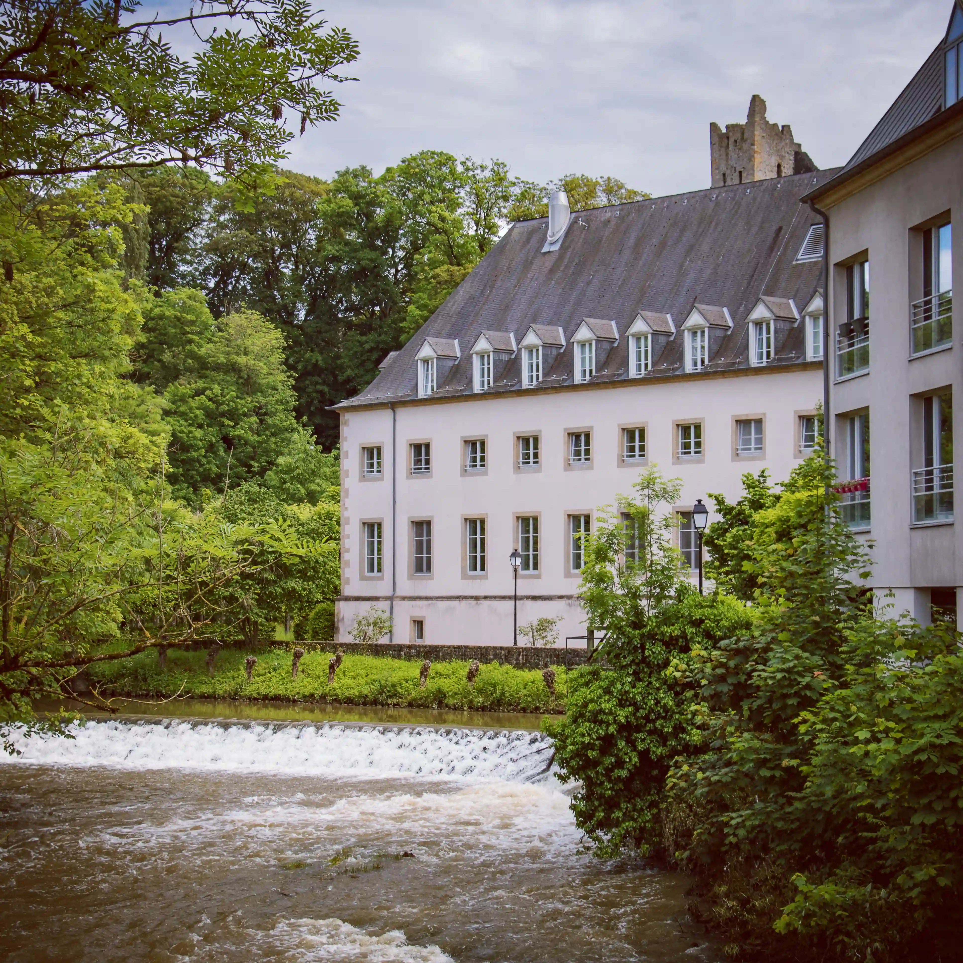 White riverside building with tall roof beside a small waterfall in Luxembourg City.