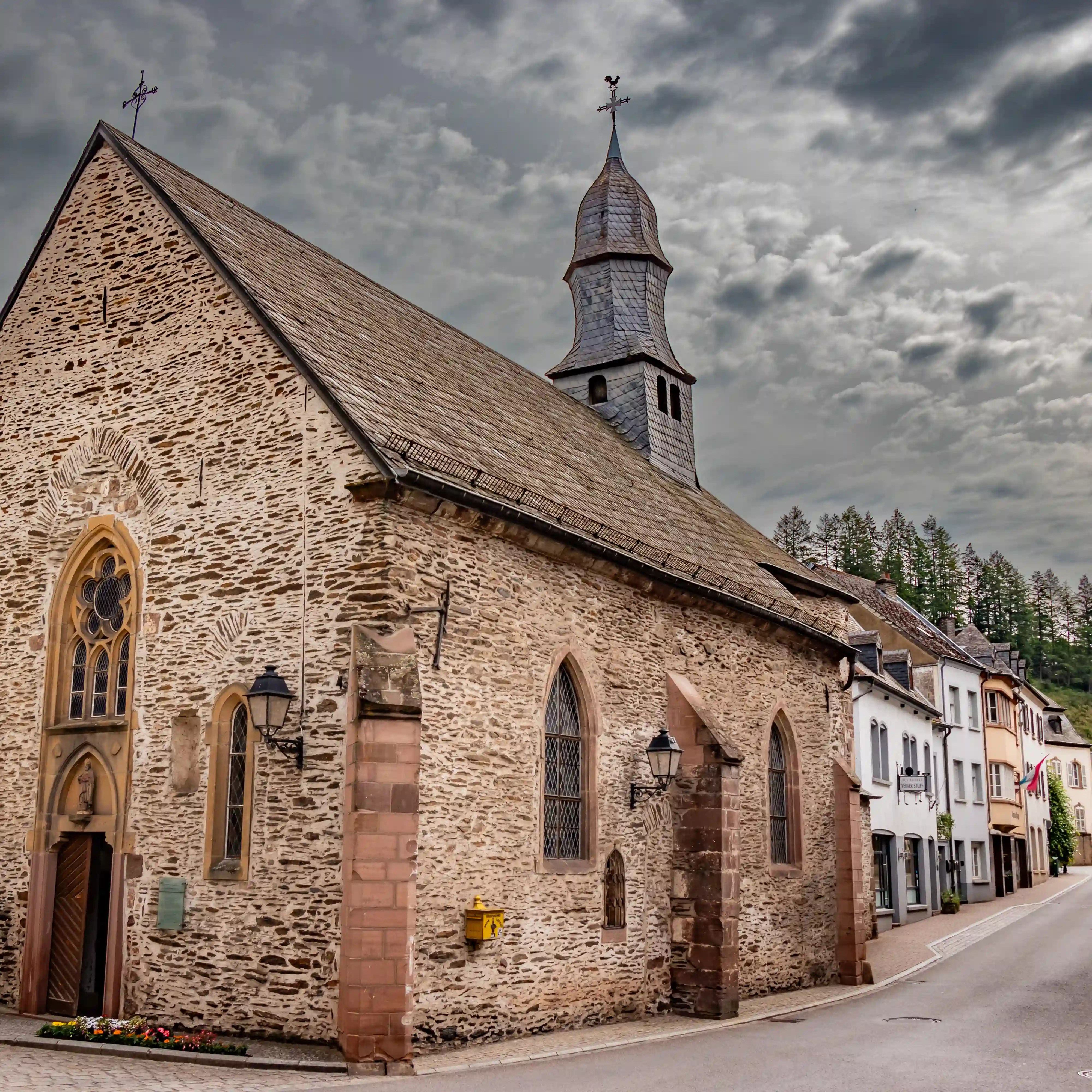 Stone Parish Church of St. Nicholas in Vianden, Luxembourg, with Gothic-style windows and a slate spire.