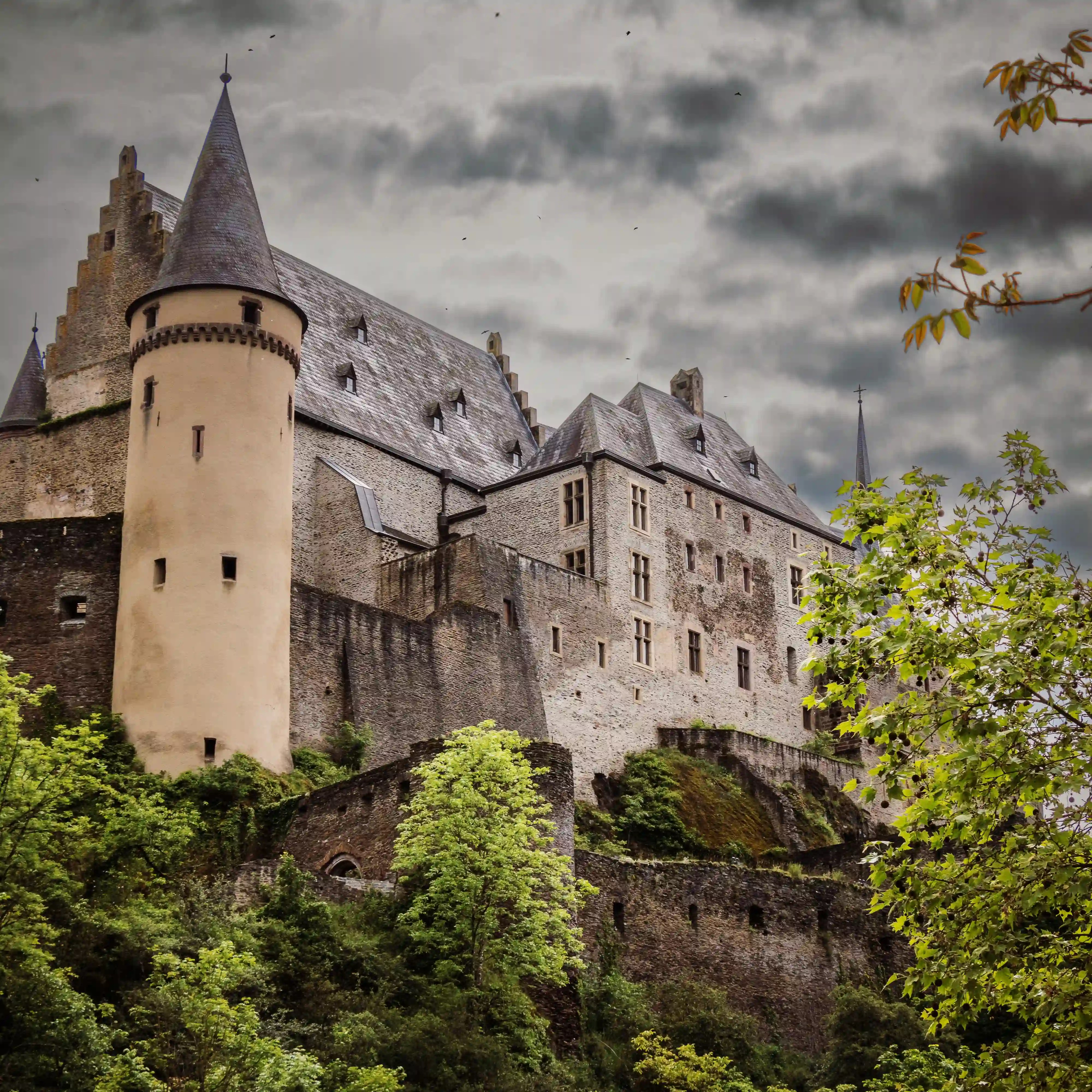 Tower and fortified walls of Vianden Castle rising against a cloudy sky.