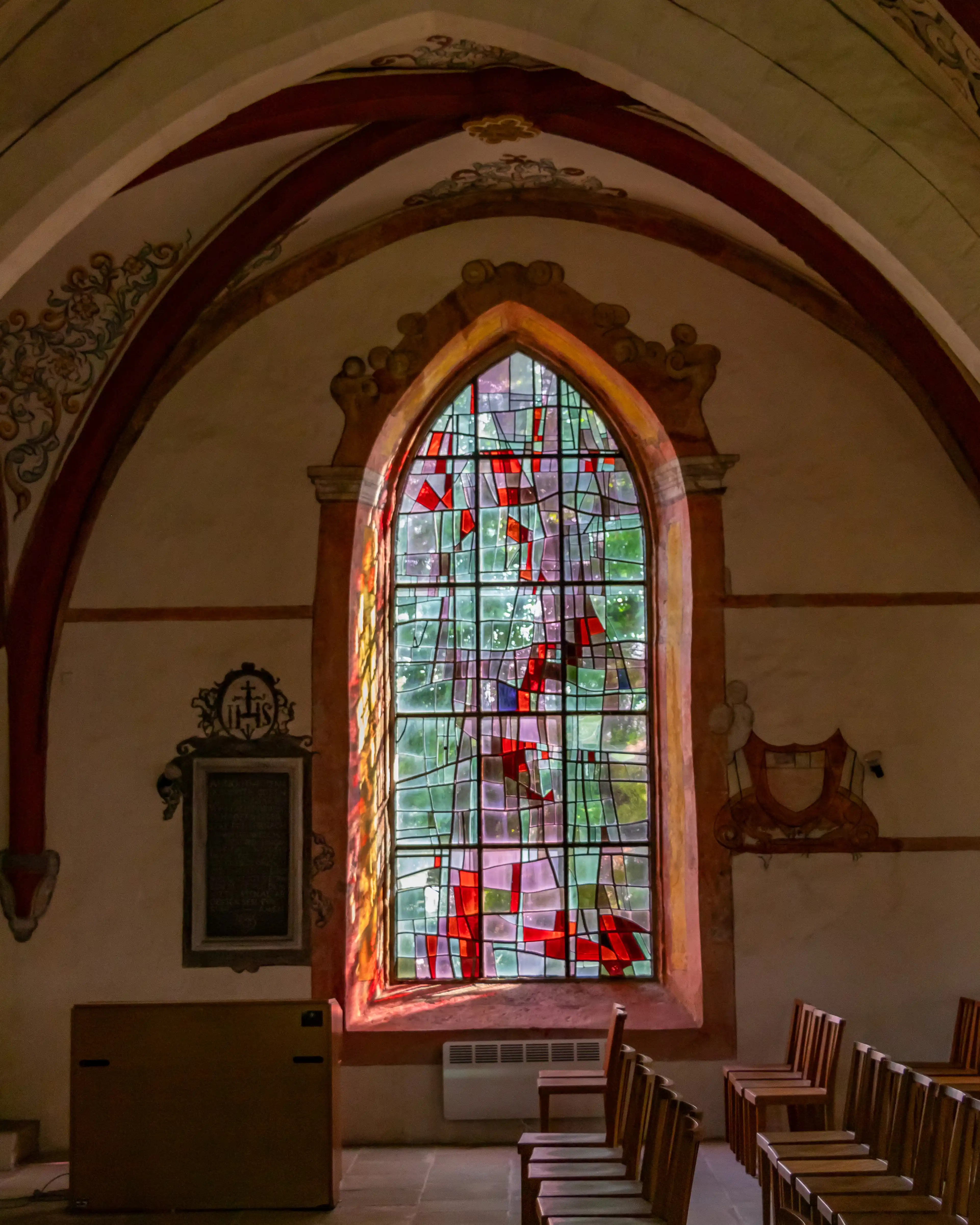Full view of an arched stained glass window with chairs and fresco details in the Church of Saints Peter and Paul.