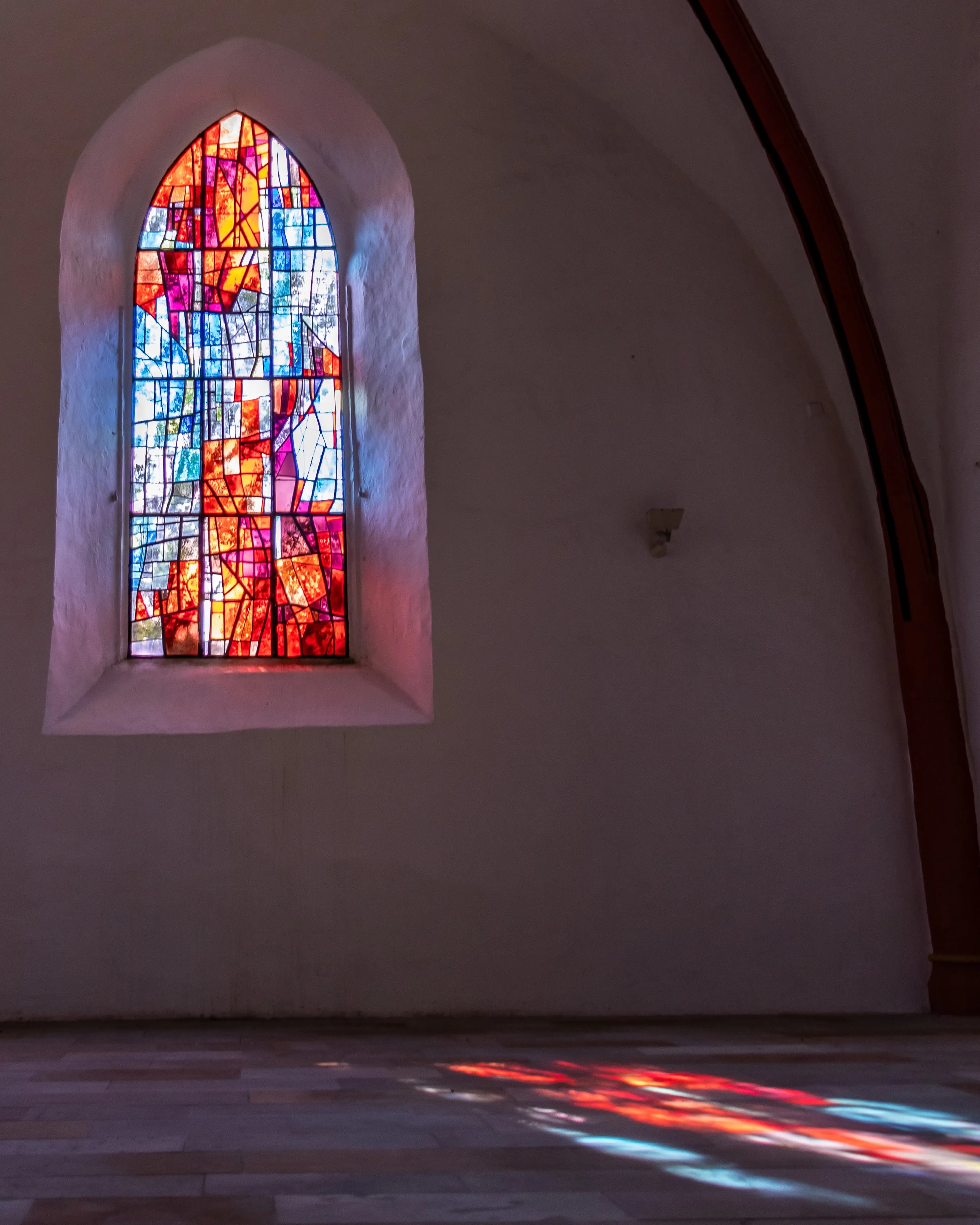 Abstract stained glass window in the Church of Saints Peter and Paul with red and blue patterns glowing in sunlight.
