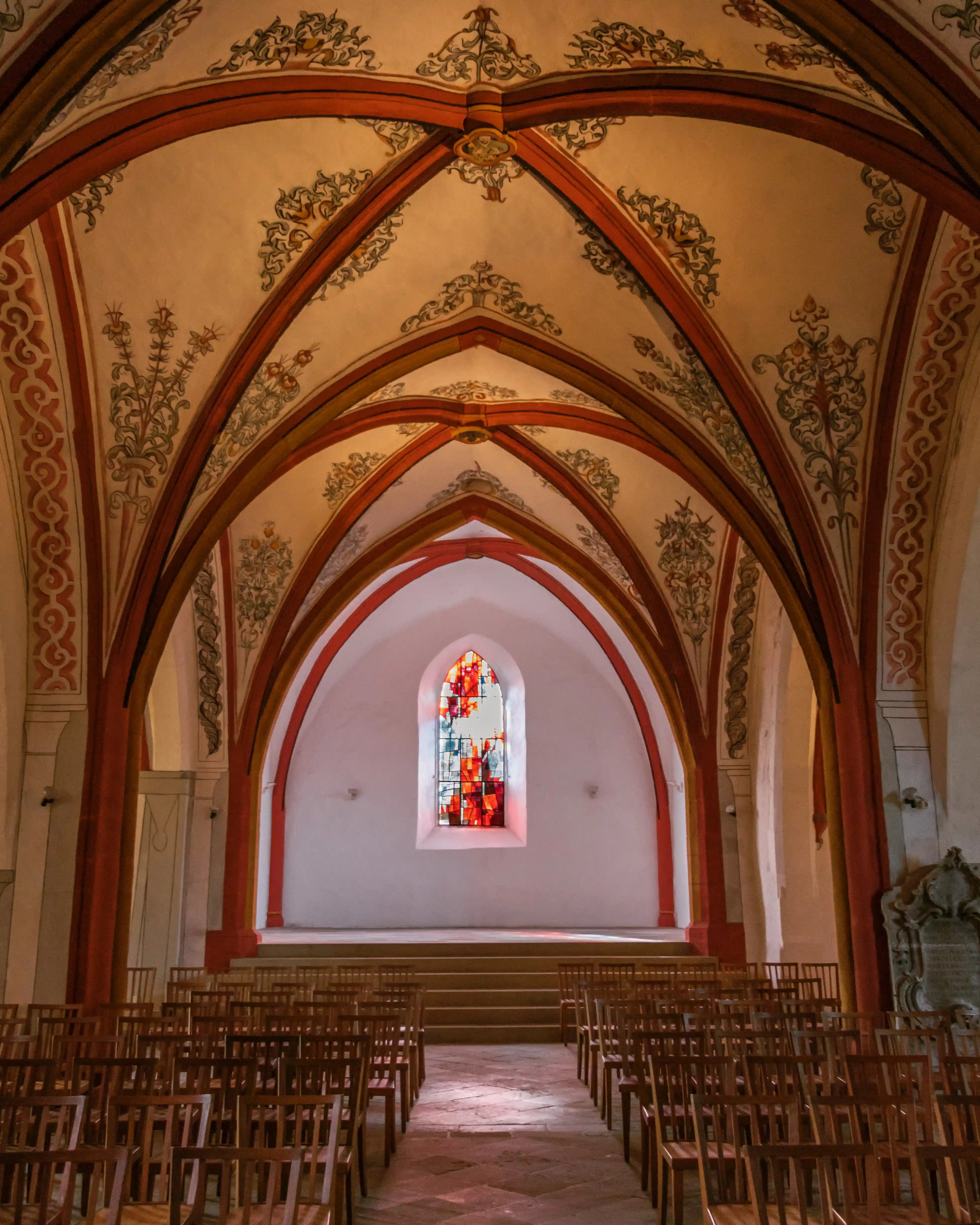 Gothic vaulted ceiling with red arches and a stained glass window at the far end of the Church of Saints Peter and Paul in Echternach.