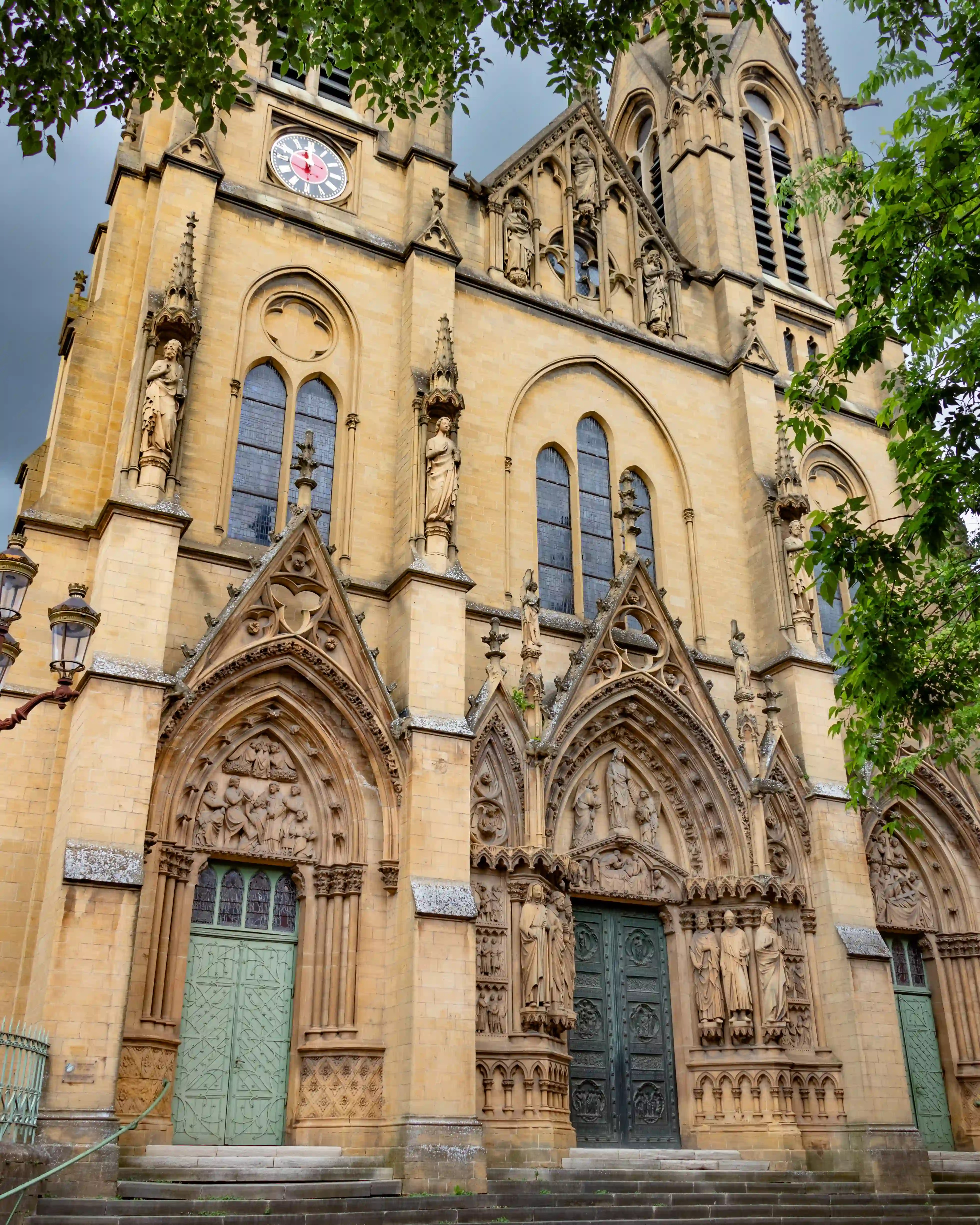 The intricate Gothic façade of Église Sainte-Ségolène in Metz with ornate statues and arched green doors.