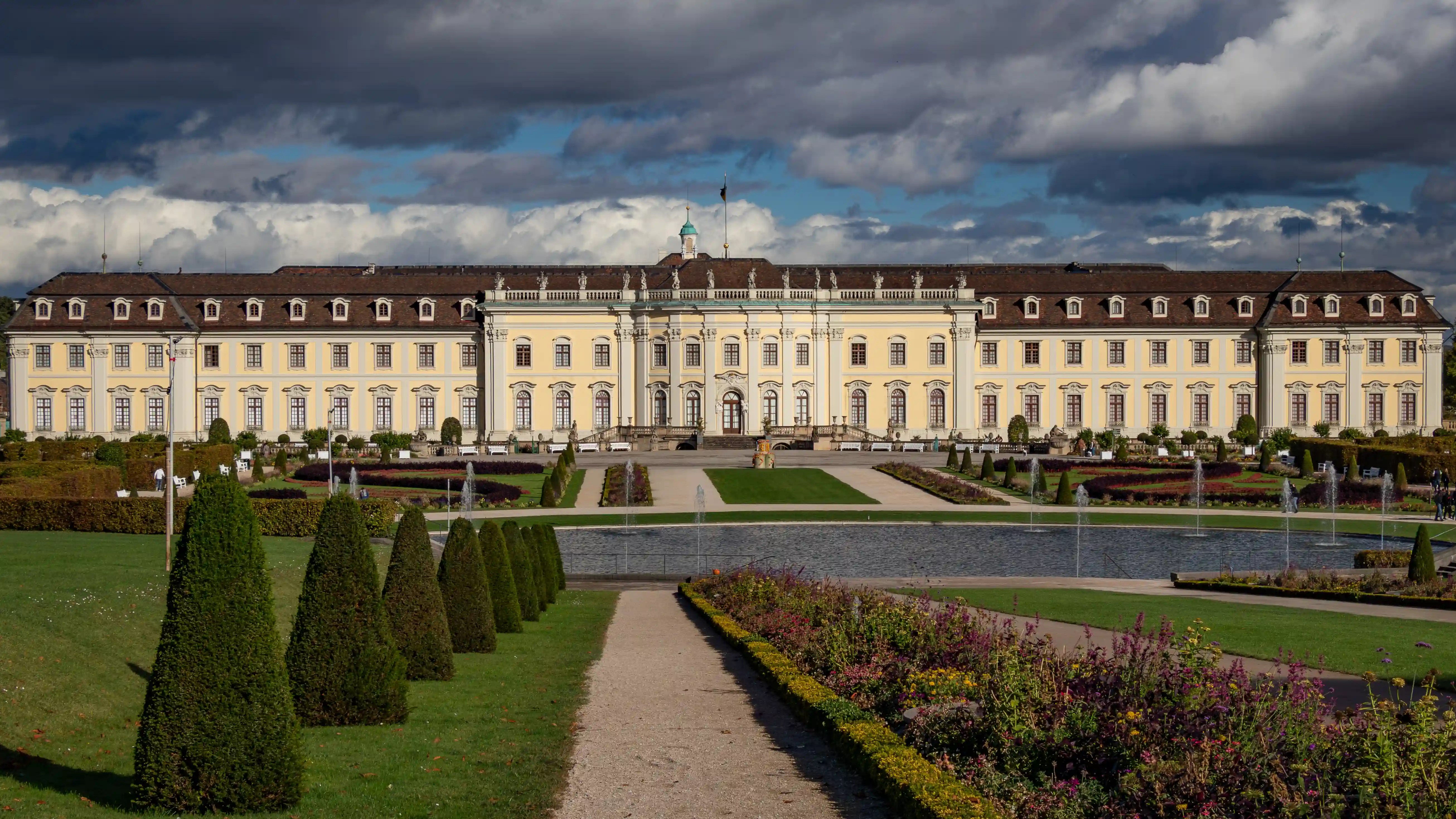 Wide view of Ludwigsburg Palace with fountains, trimmed hedges, and flower beds in the foreground.