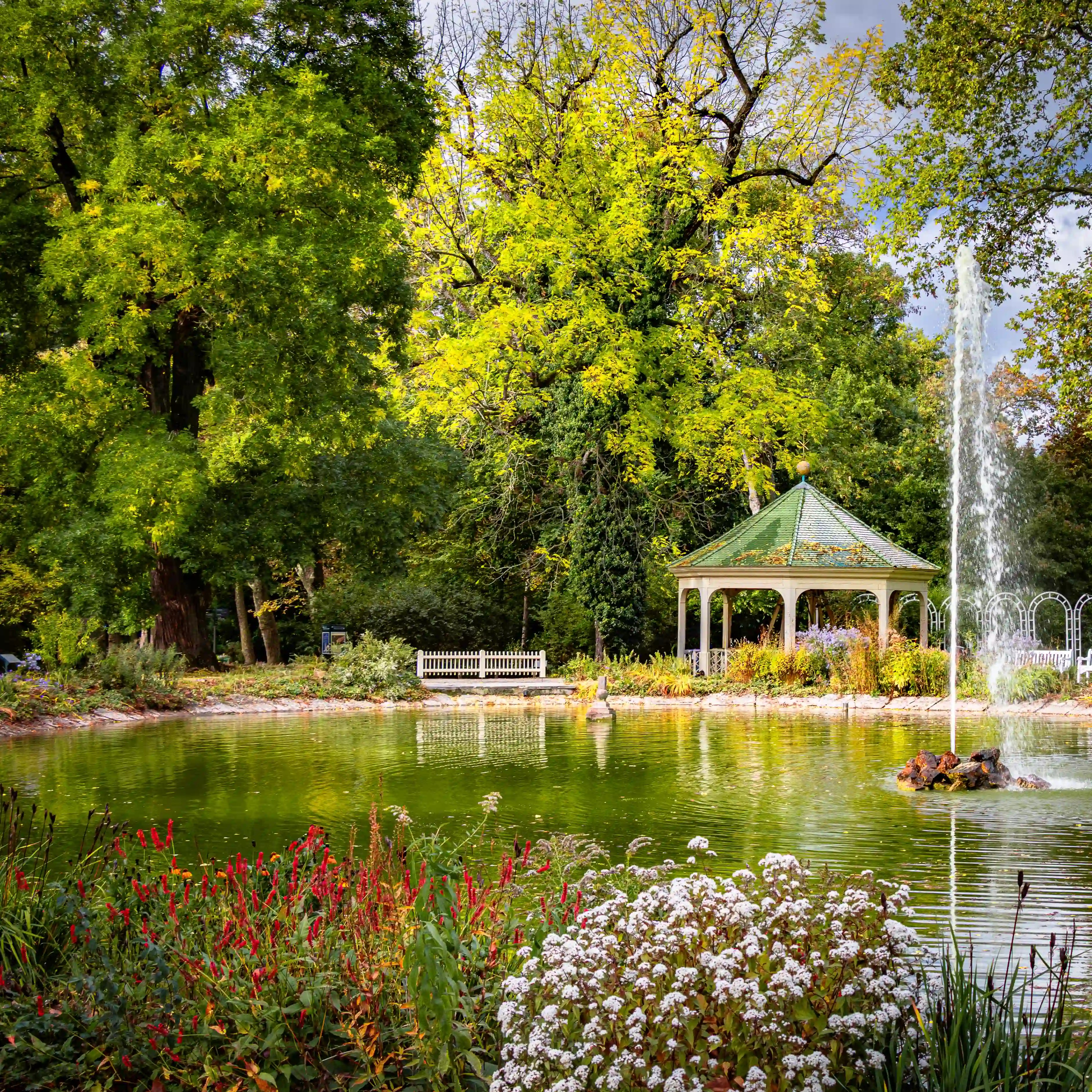 Small lake with fountain, flower beds, and a green-roofed pavilion in the gardens of Ludwigsburg Palace.
